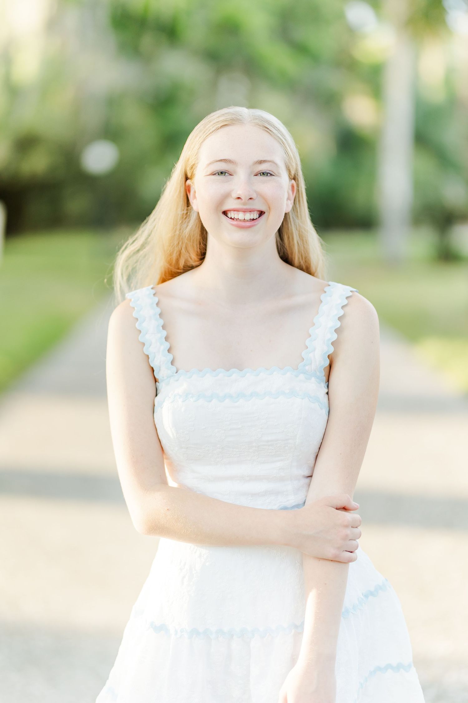 A person in a white summer dress stands outdoors in a garden setting with soft natural lighting.