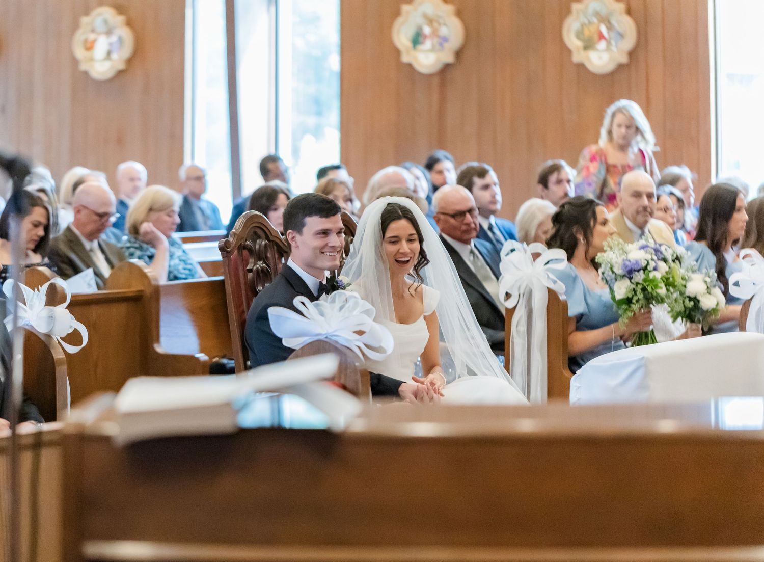 Wedding guests seated in wooden church pews during ceremony.