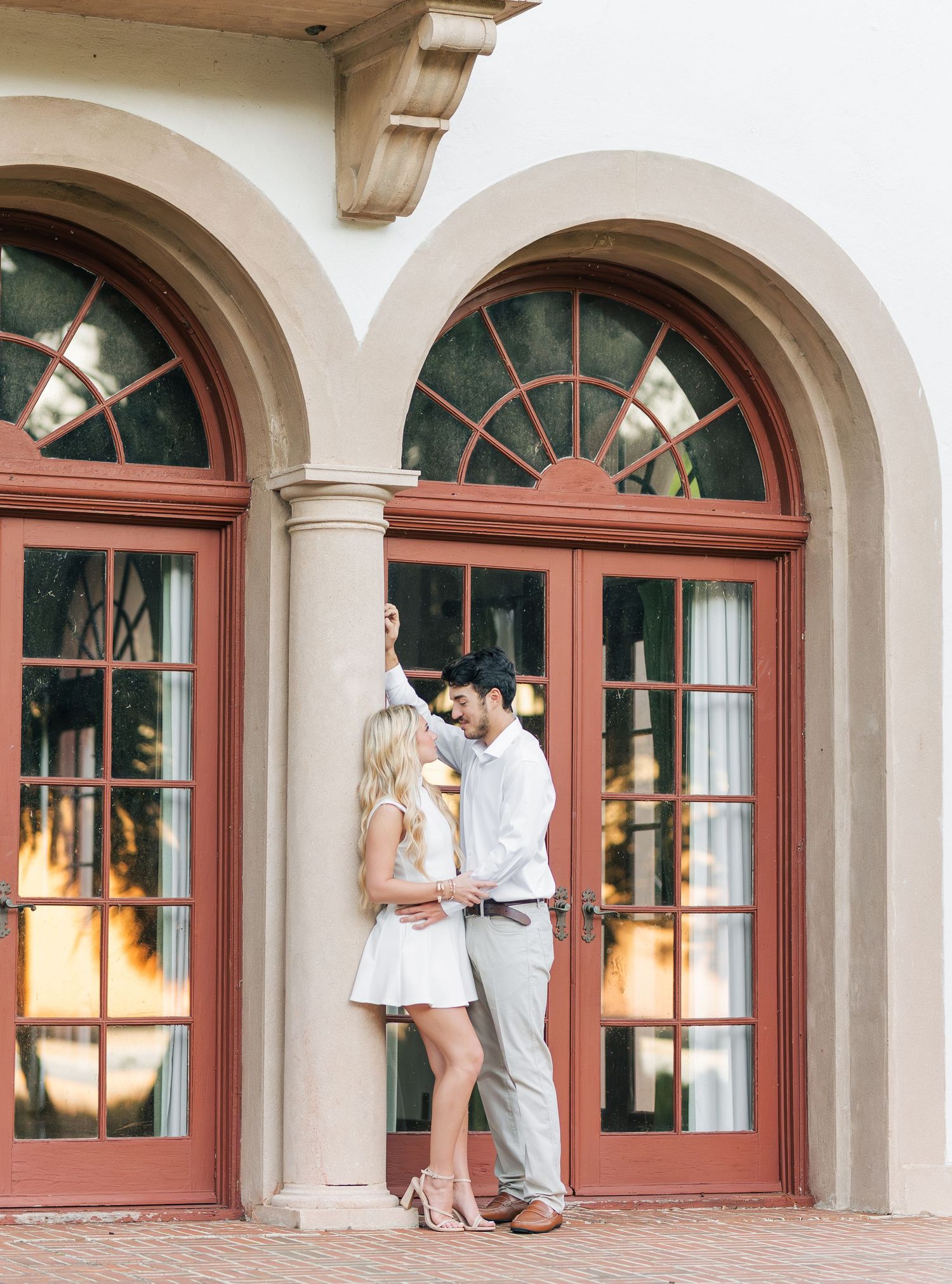 A romantic couple poses in an elegant arched doorway with terracotta-colored trim.
