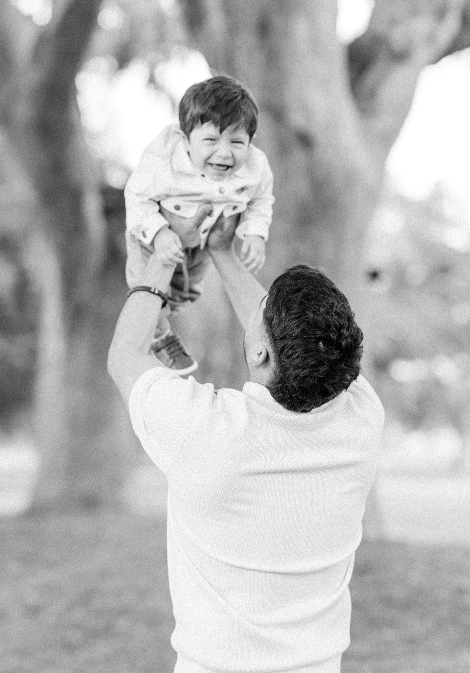 Black and white photo series of playful parent-child interactions outdoors showing joyful lifts and embraces.