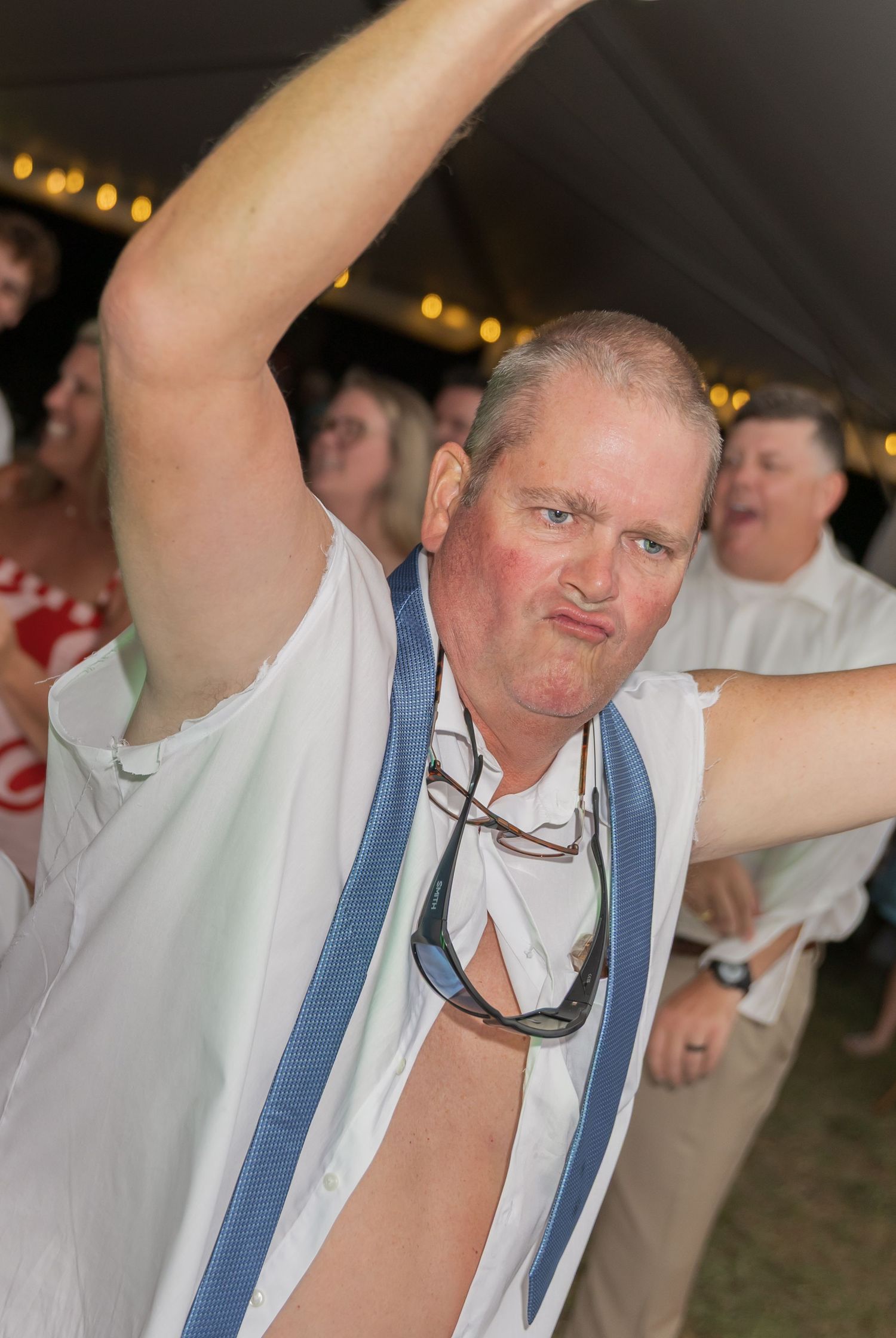 Man in suspenders making funny faces while dancing at a wedding reception.