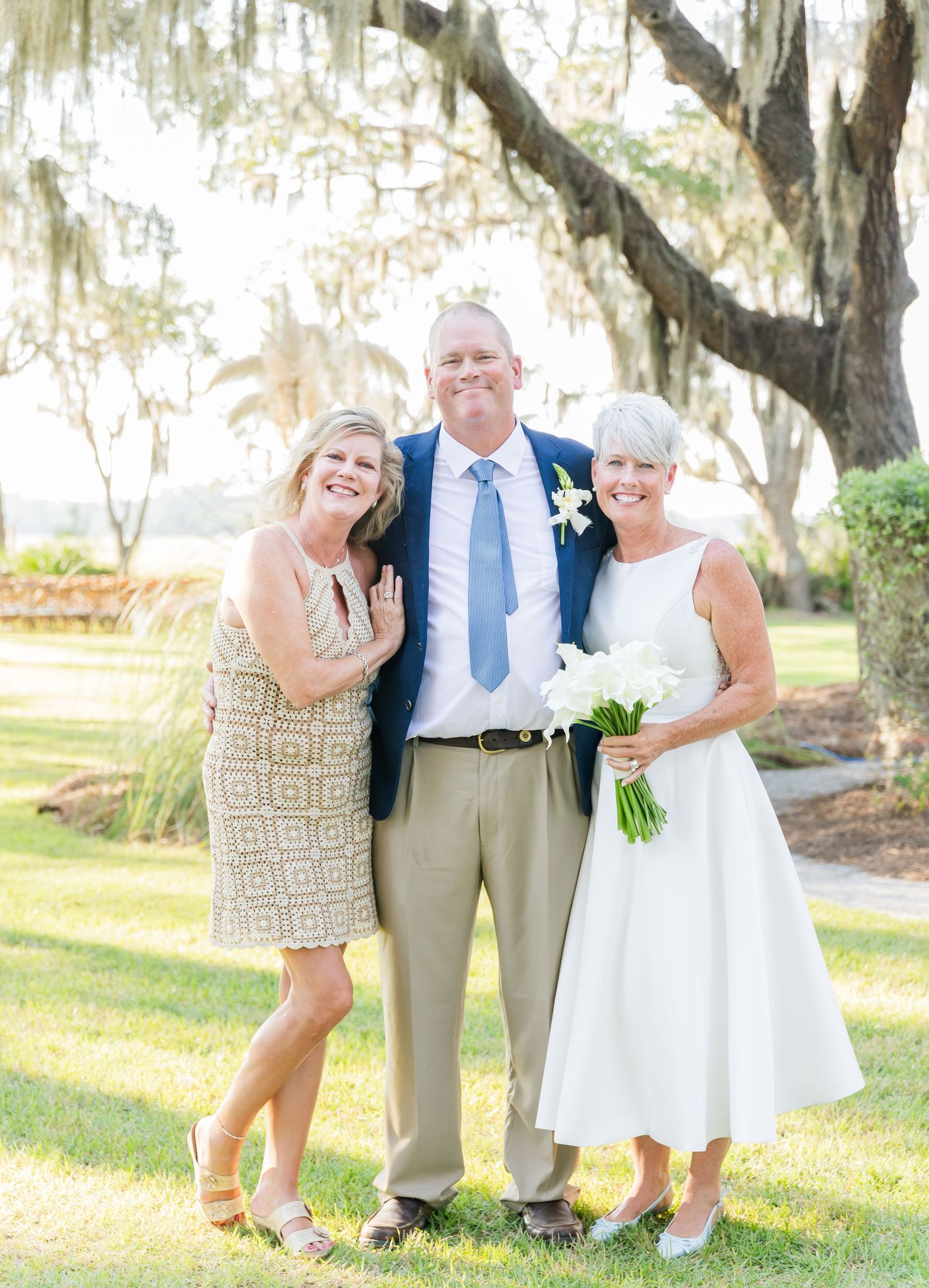 Three people pose together under Spanish moss draped trees at an outdoor wedding venue on a sunny day.