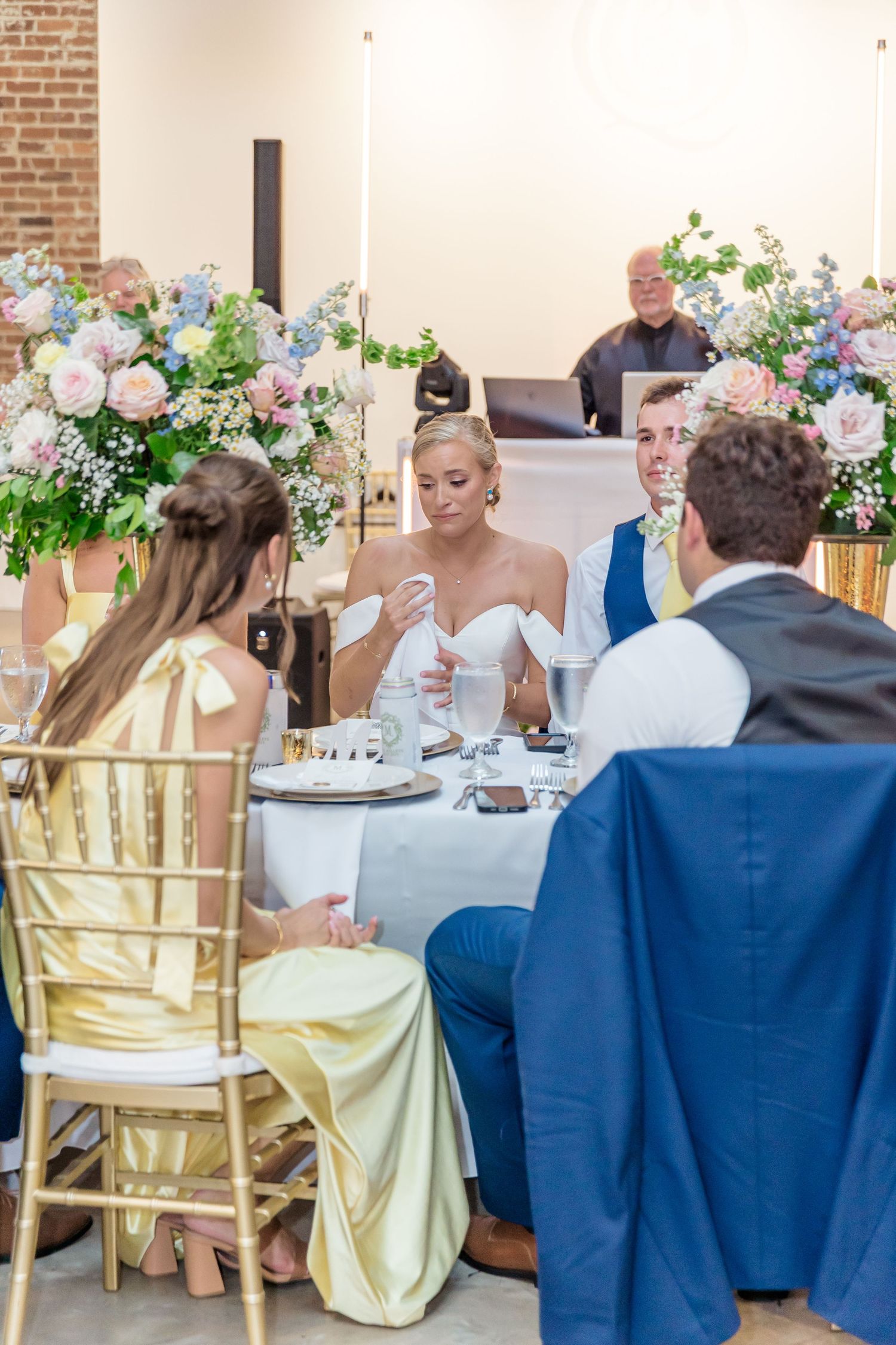 Wedding reception table setup with guests seated in gold chairs enjoying a meal in an industrial-chic venue.