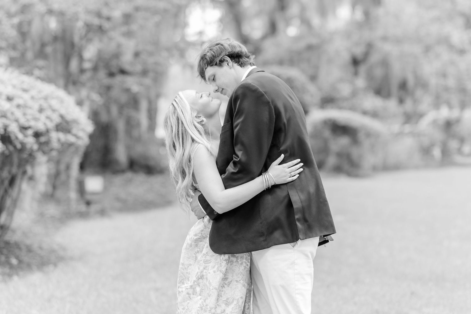 A romantic black and white photograph of a couple embracing outdoors in a garden setting.