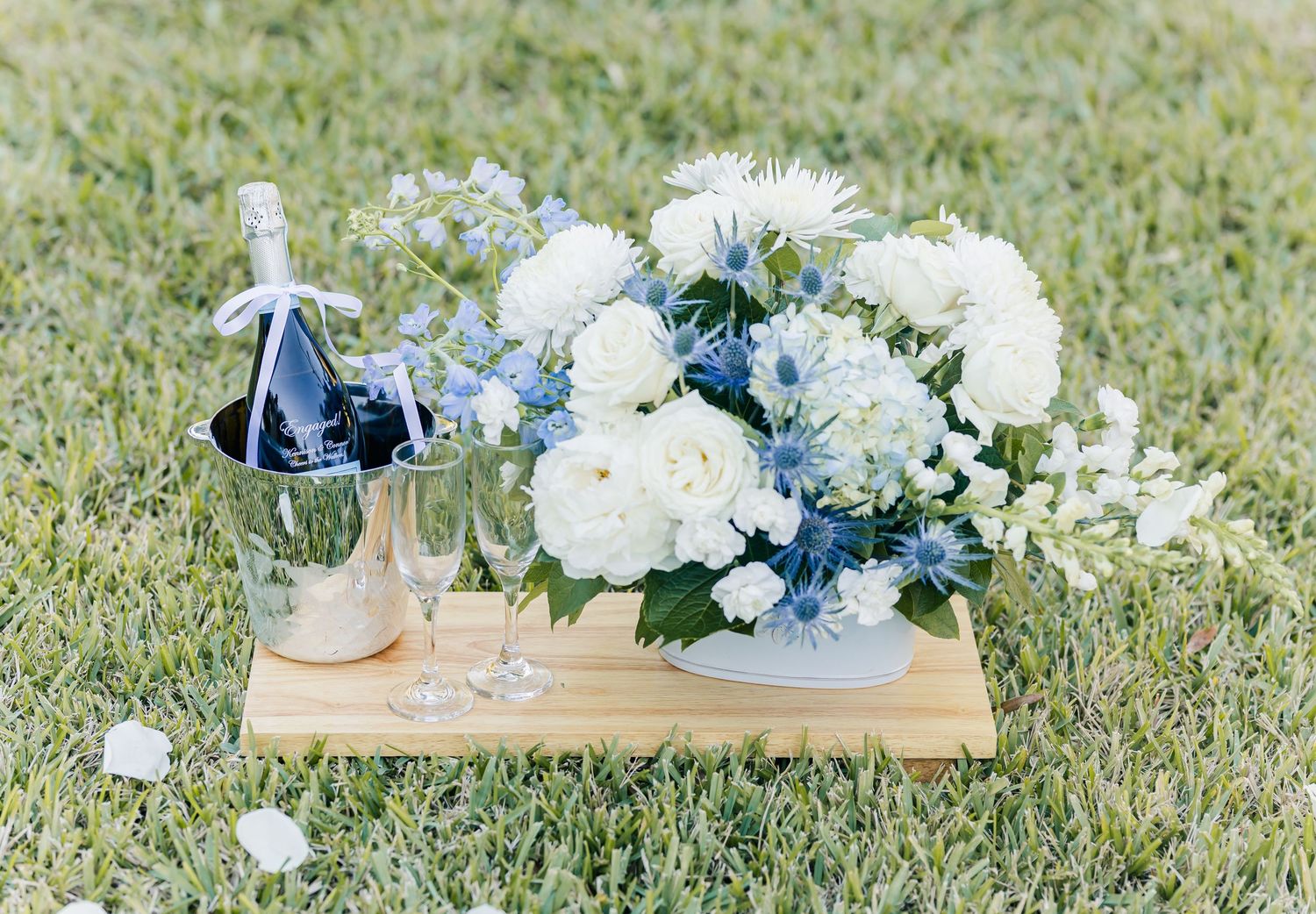 Elegant wedding table decor with white floral arrangements and glassware displayed on wooden boards in grass.
