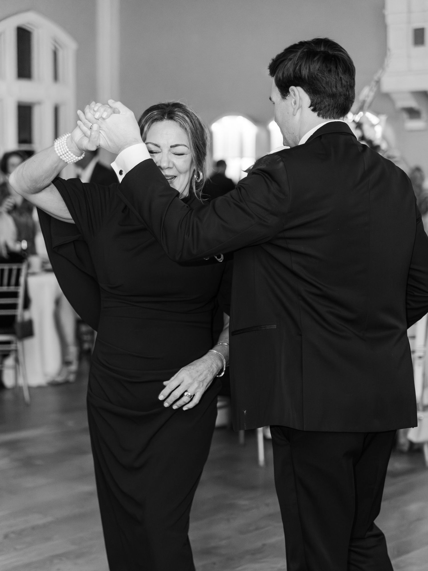 Couple shares a joyful dance at wedding reception in black and white photo, twirling elegantly.