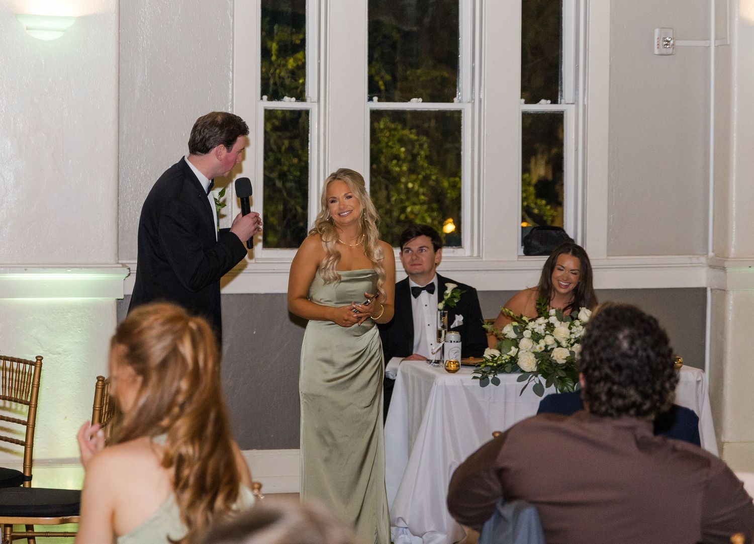 Bride and groom share a toast with wedding party during elegant indoor reception ceremony.