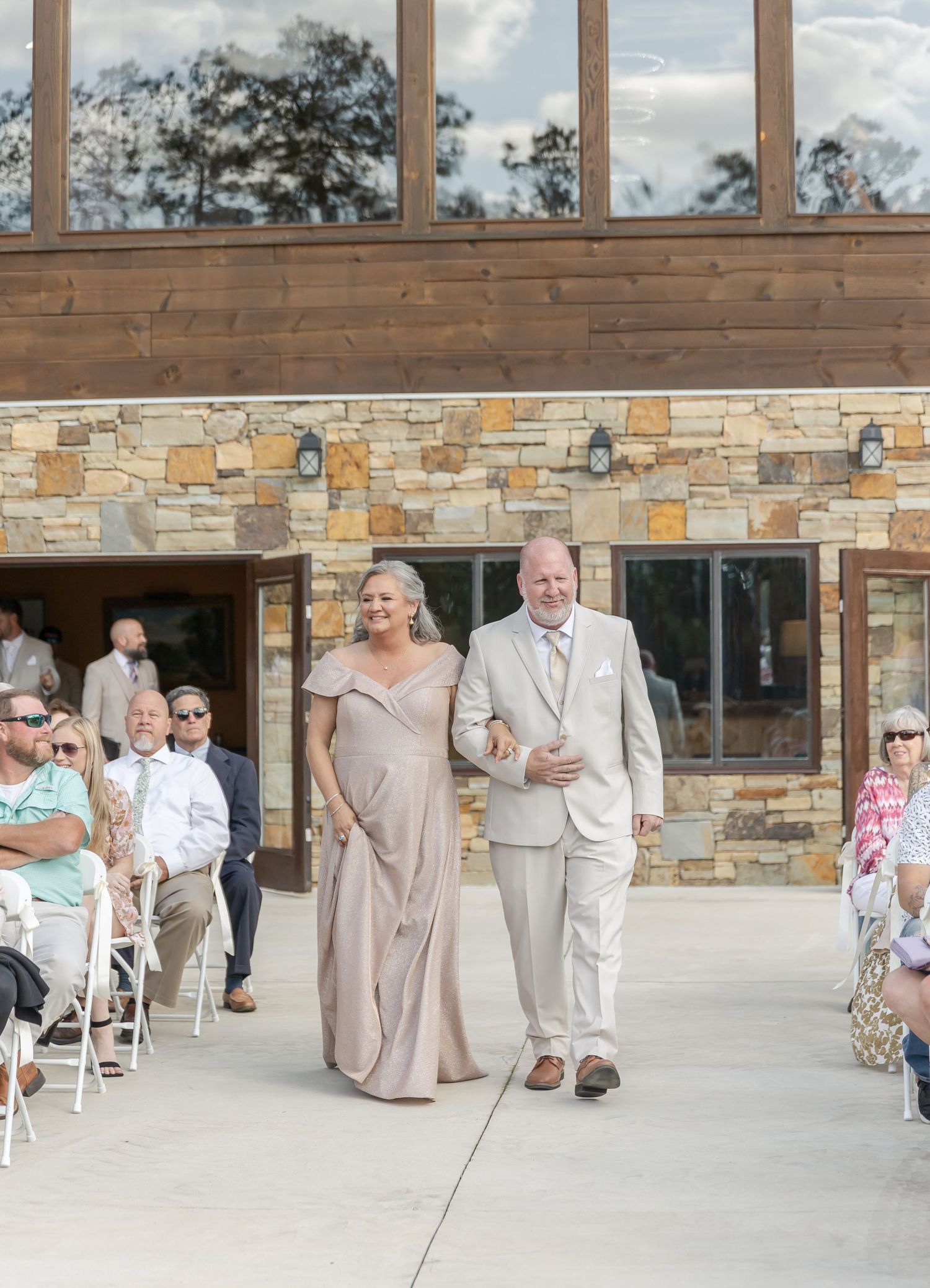 Elegant procession at stone venue with guests seated in white chairs during wedding ceremony.