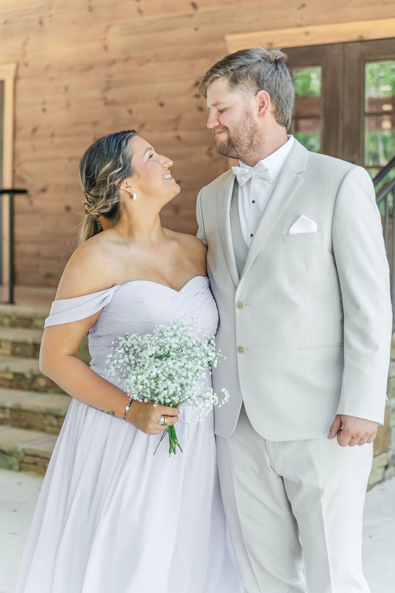 Couple shares intimate moment in formal wedding attire on rustic wooden porch.