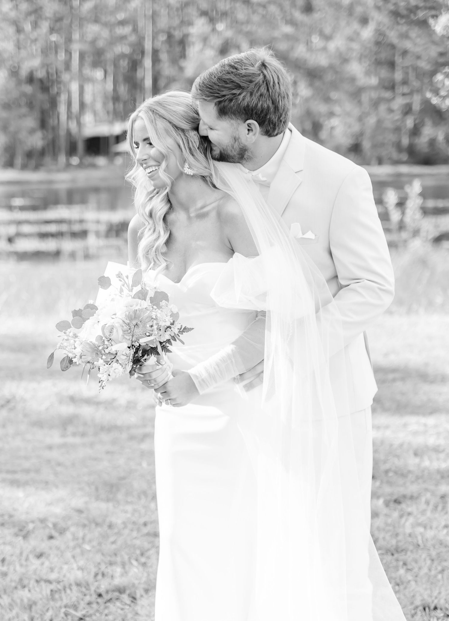 Black and white portrait of newlyweds sharing tender moment with floral bouquet.