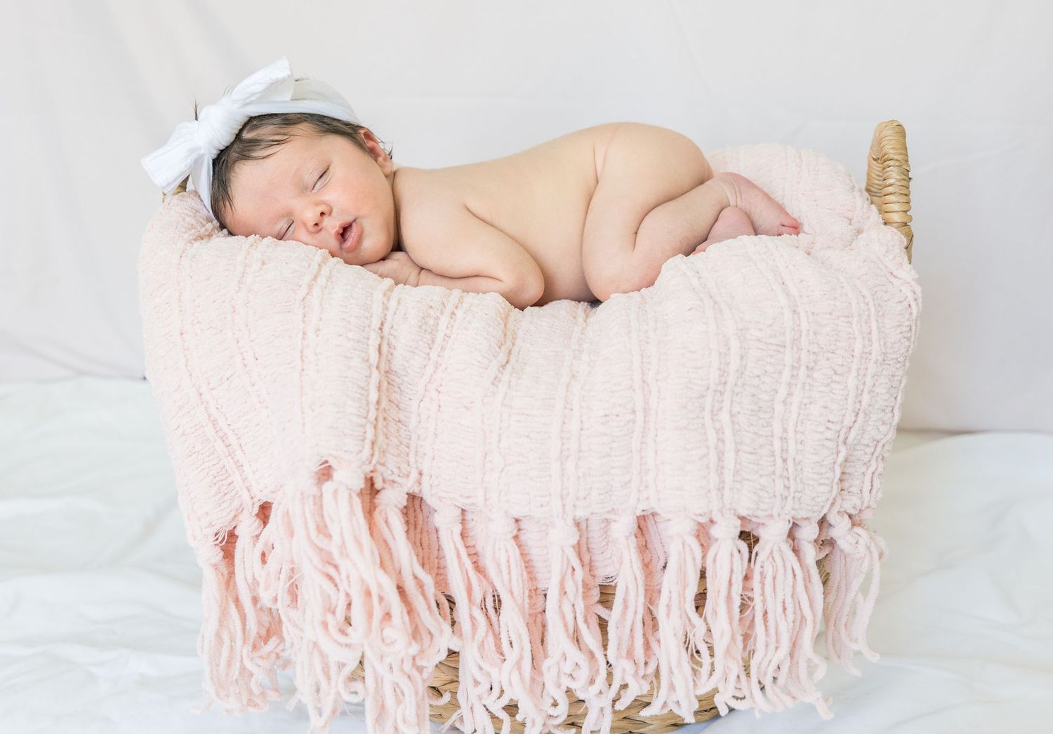 Sleeping baby in basket draped with pink fringed blanket.