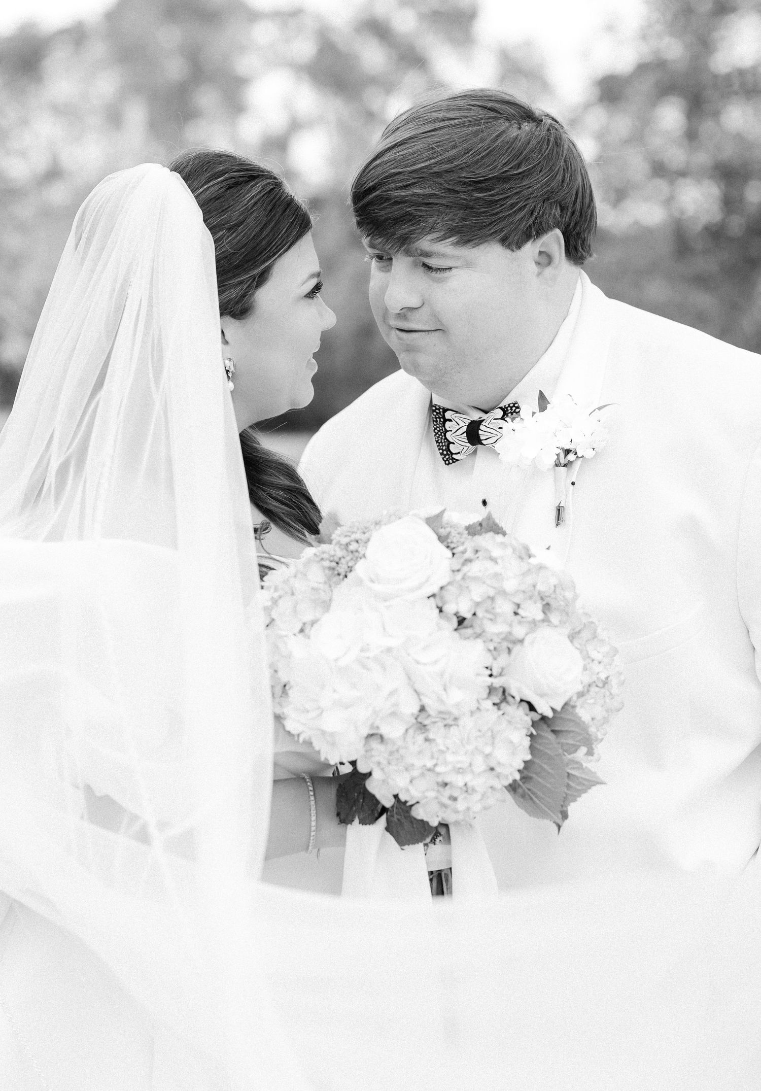 Black and white romantic portrait of bride and groom sharing a tender moment beneath flowing wedding veil.