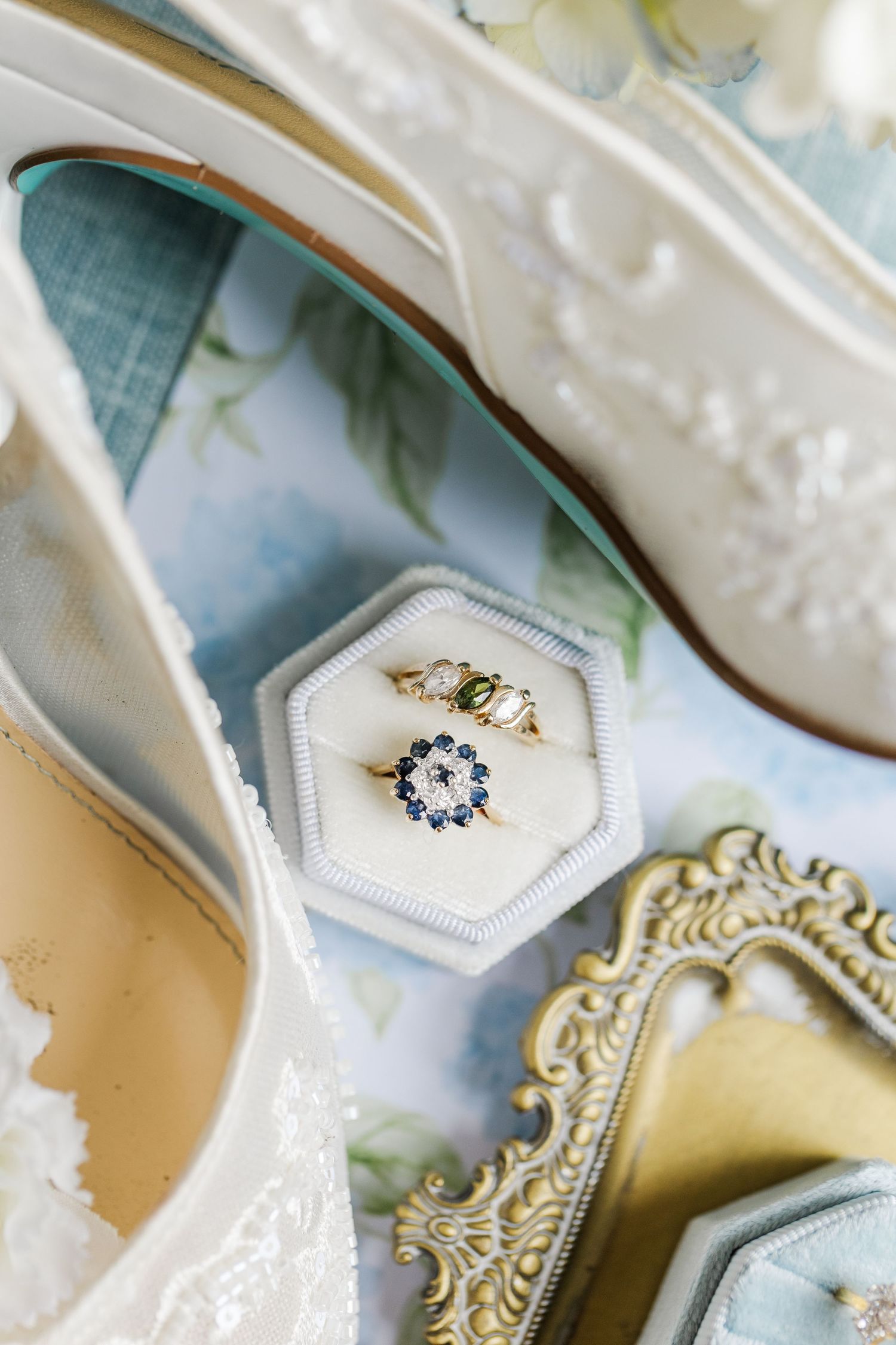 Vintage sapphire halo and green stone gold rings displayed in hexagonal white velvet box with bridal heels.