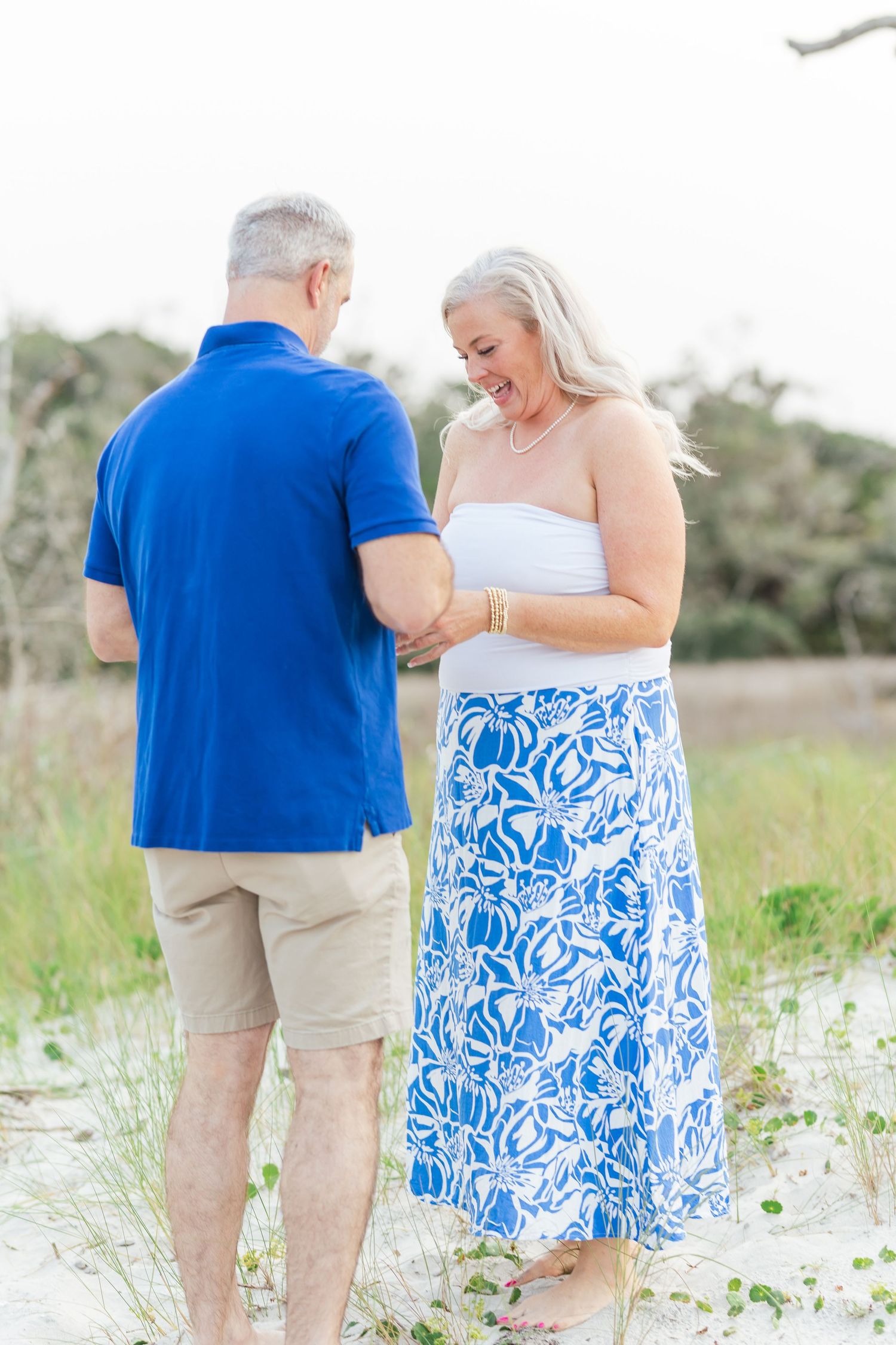 A couple in coordinating blue and white outfits walks together on a sandy beach during a sunset photoshoot.