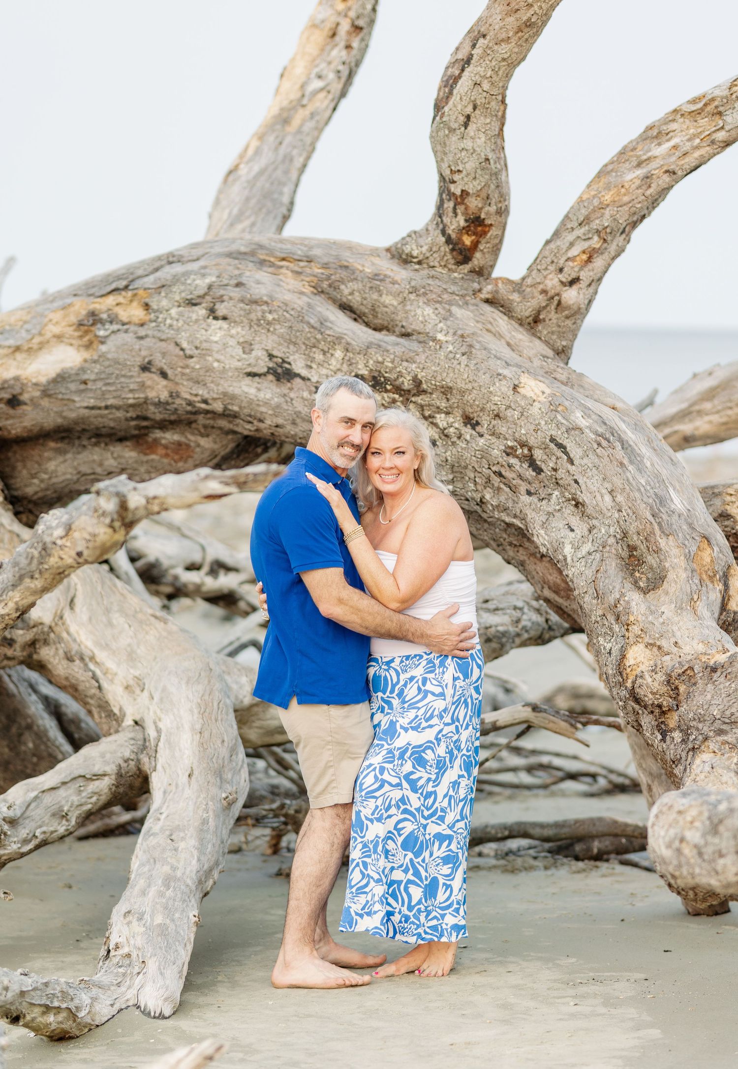 A romantic beach portrait amid driftwood and sandy shores at Jekyll Island, with blue and white coastal attire.
