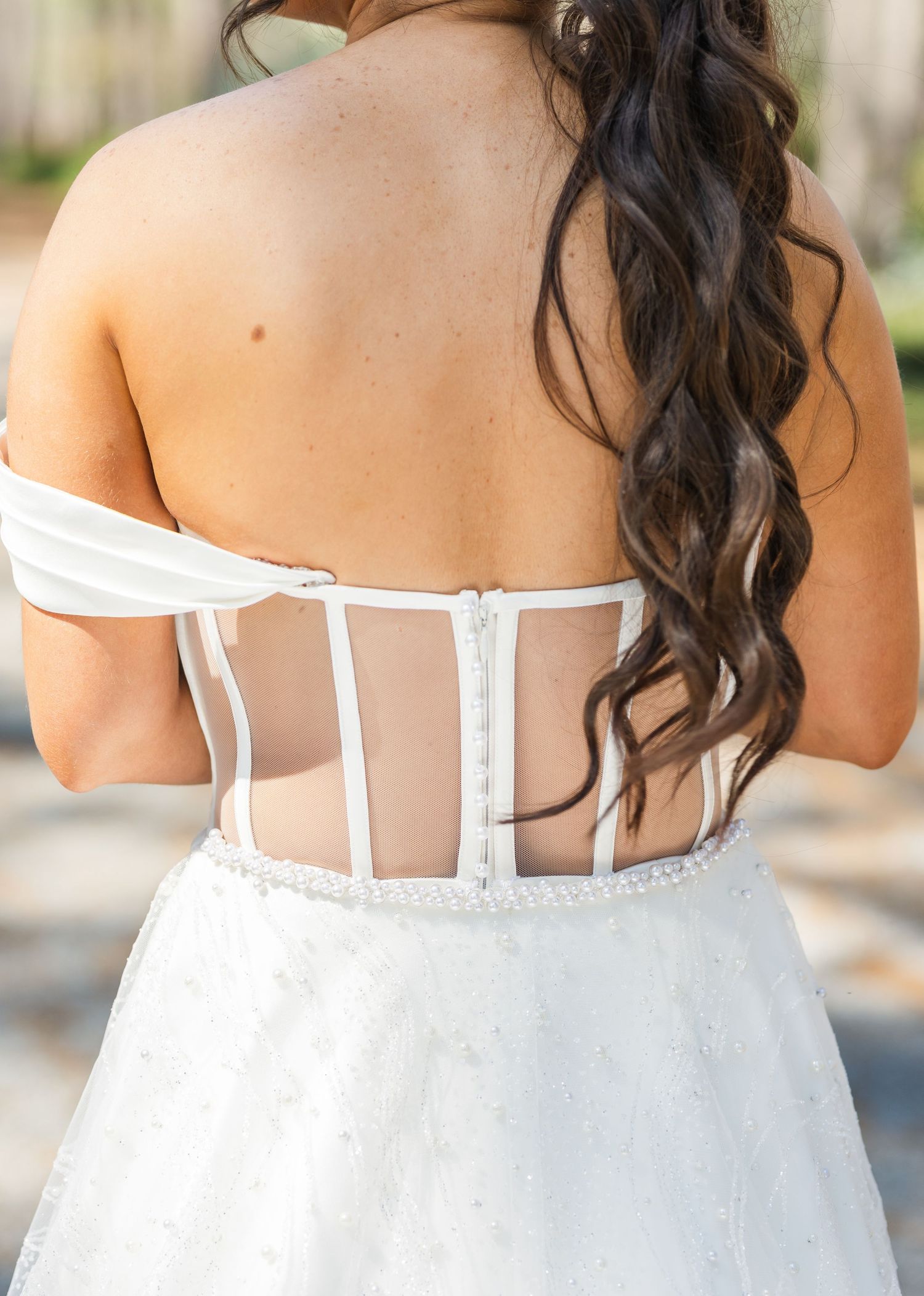 Back view of bride in strapless corset wedding gown with sheer boning detail and off-shoulder straps.