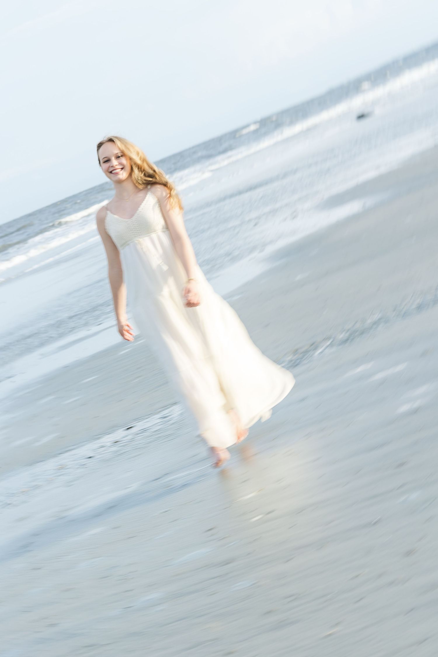 Dreamy beach photoshoot with soft focus of someone in a flowing white dress by the ocean.