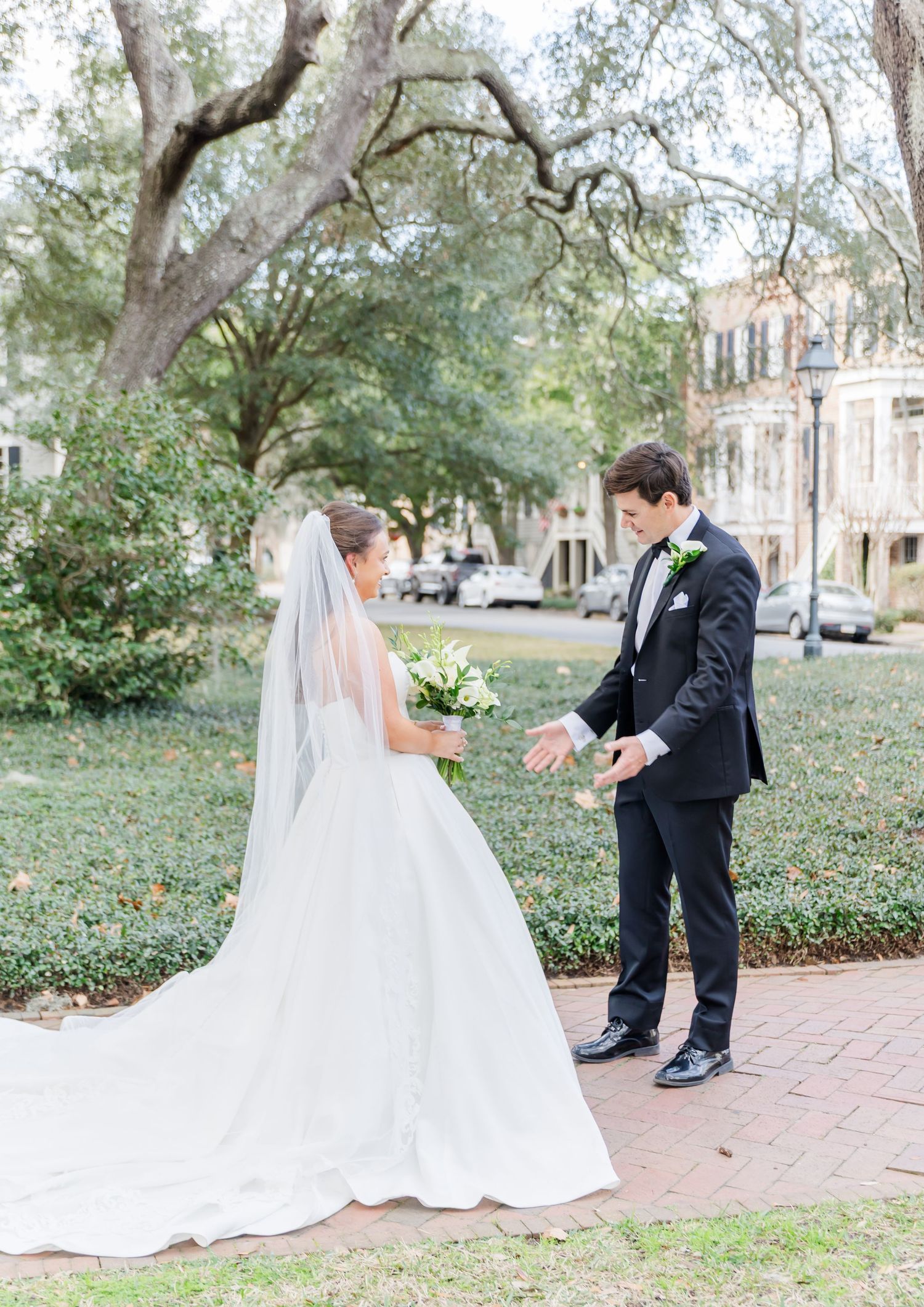 First look wedding moment captured on brick pathway surrounded by trees and historic buildings.