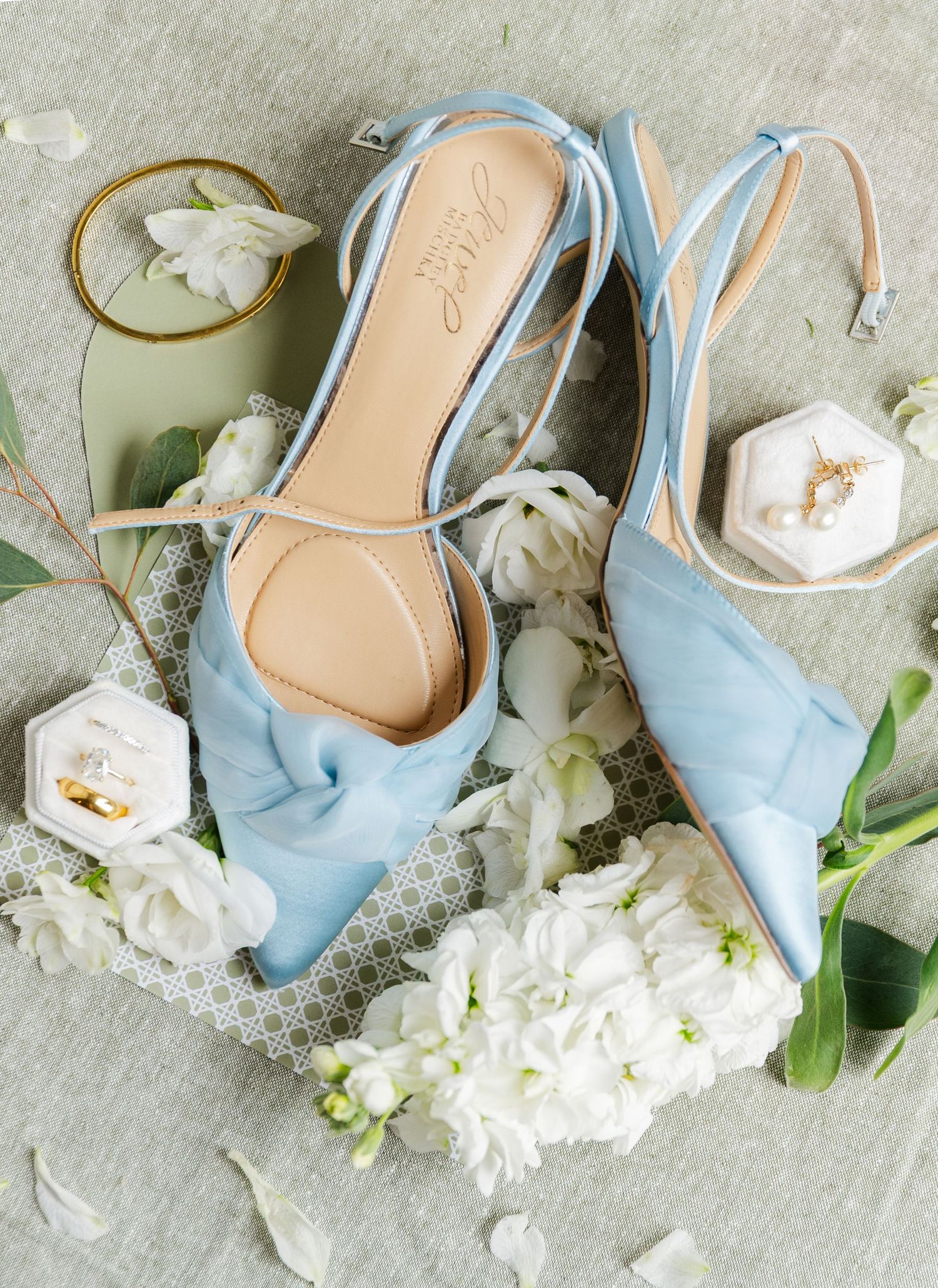 Light blue bridal shoes with white flowers arranged in a row on grey surface.