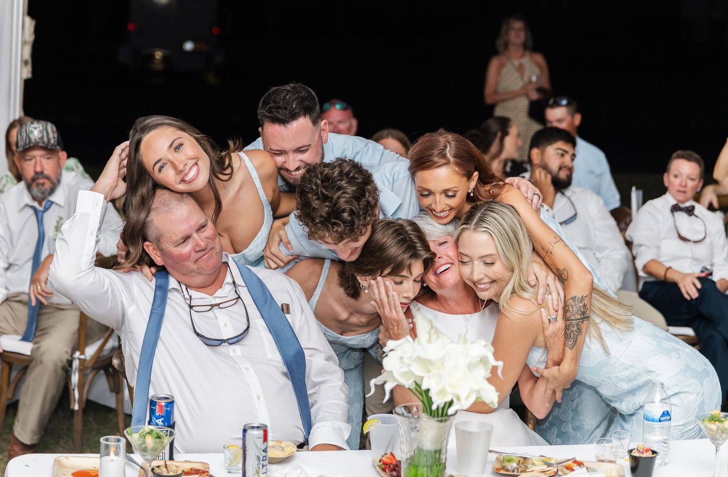 Wedding guests laughing and celebrating during reception party under tent lighting.