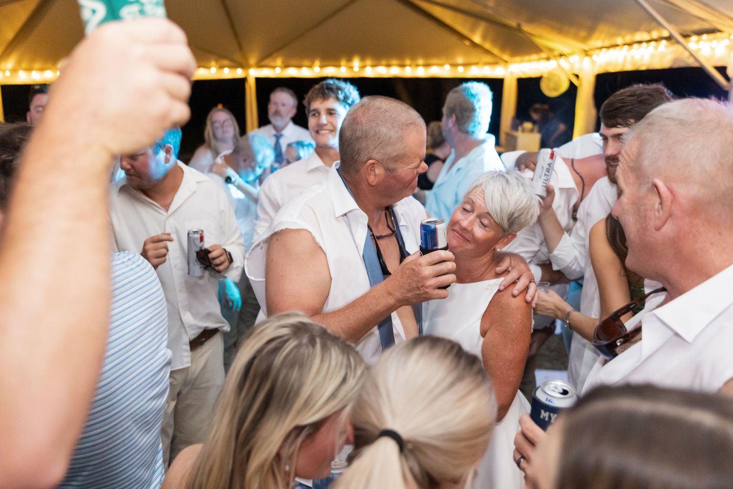 Festive crowd mingles and dances at an outdoor celebration with drinks in hand.