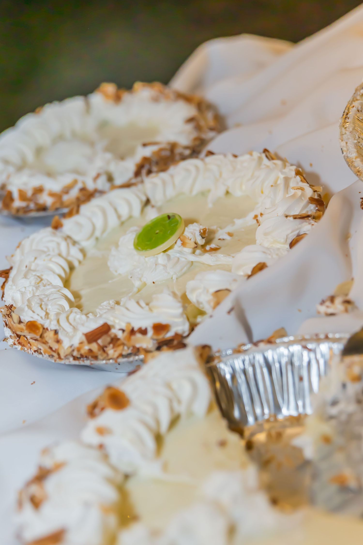 Creamy white desserts with whipped topping arranged in foil tins on a white tablecloth.