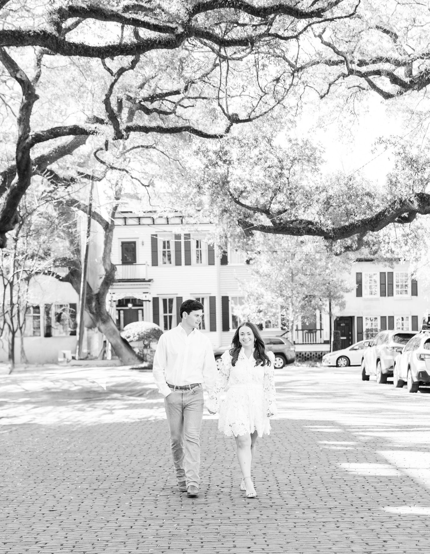 A black and white photo of a couple walking down a tree-lined street in historic Charleston.