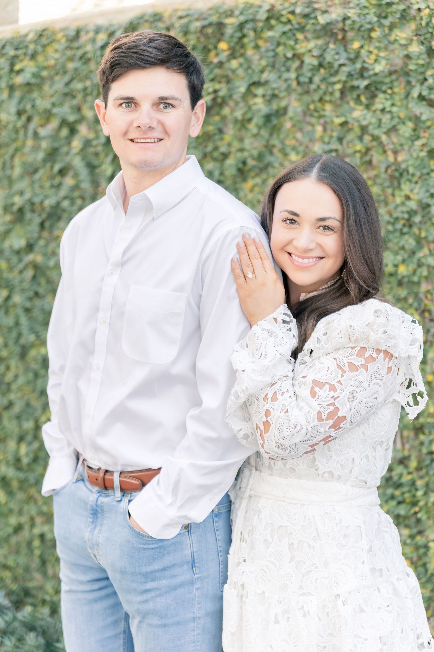 A couple poses together against a lush ivy wall backdrop in classic white and blue attire.