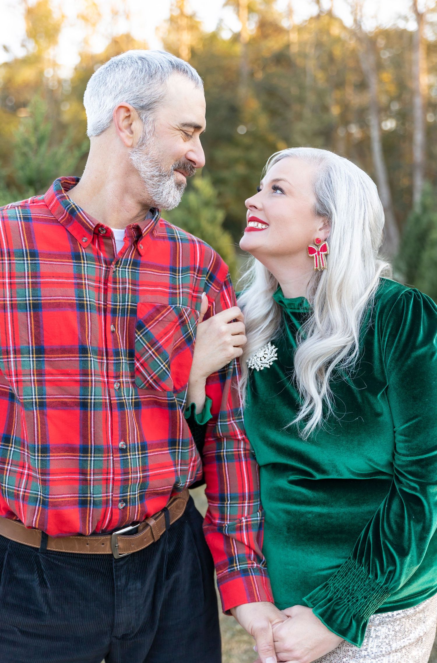 Romantic holiday photo of couple wearing plaid and velvet while sharing a joyful moment outdoors.