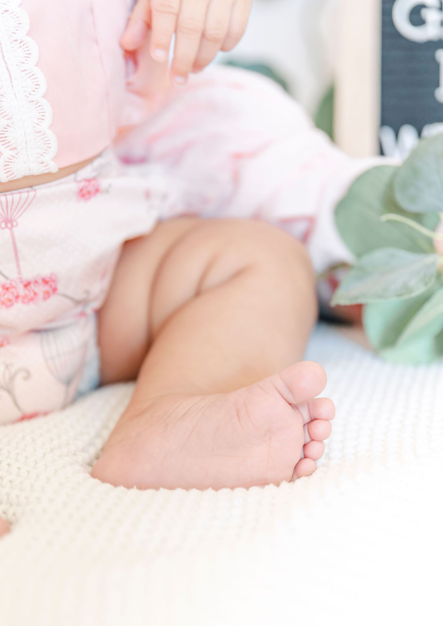 Close-up of tiny baby feet and pink ruffled clothing against white background.