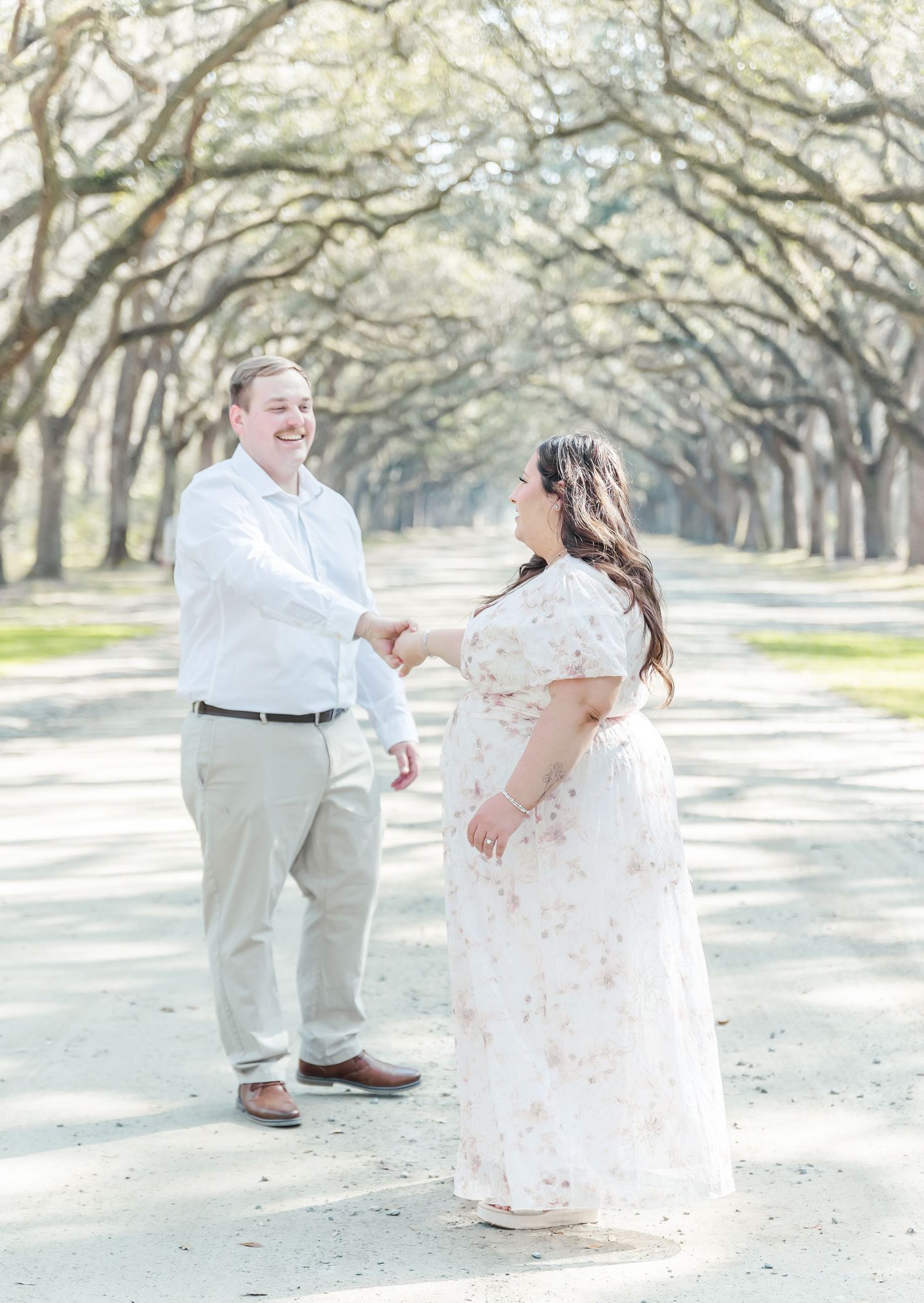 A joyful couple sharing a playful moment under a beautiful oak tree tunnel.