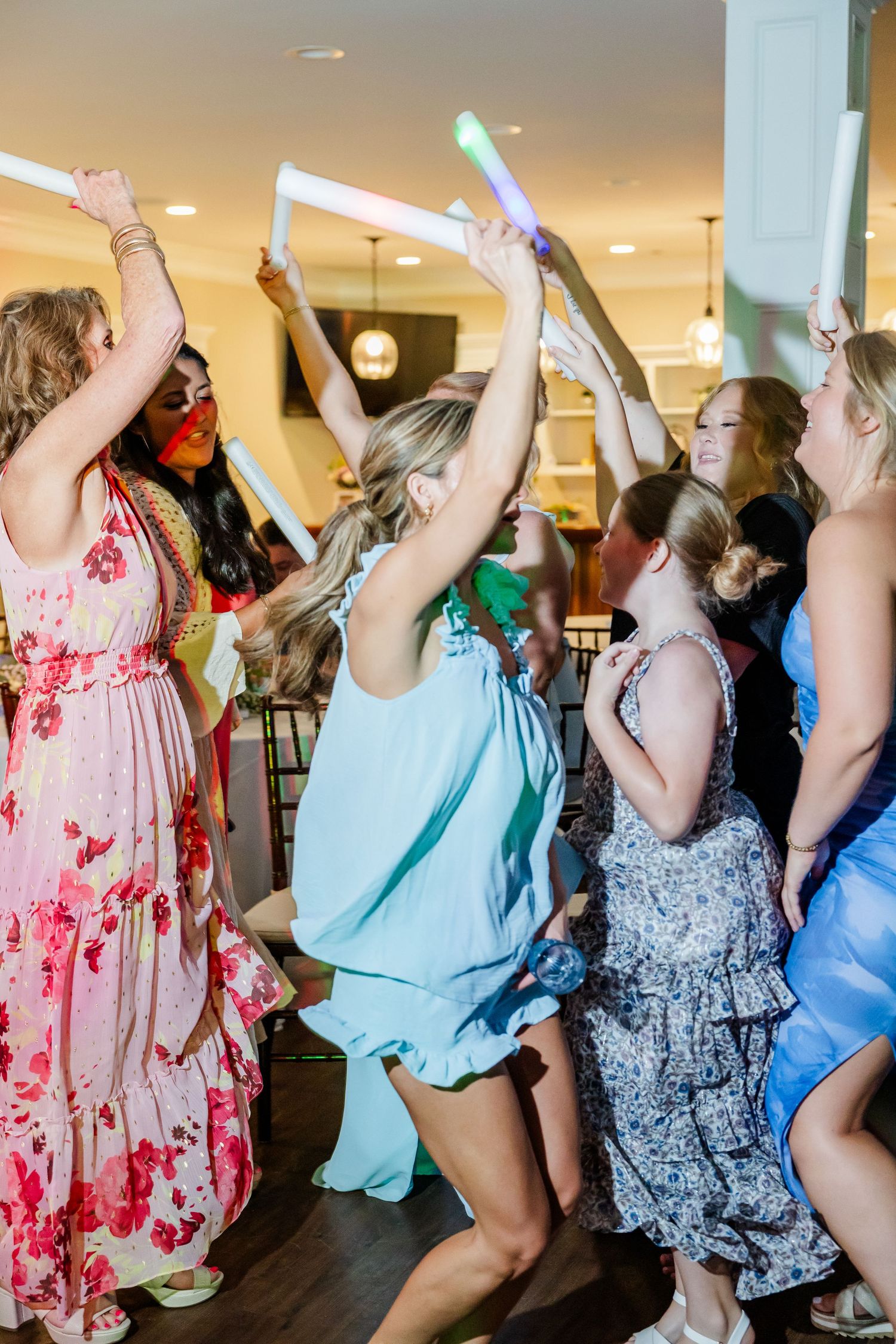 Wedding guests dance joyfully with colorful glow sticks raised at lively reception celebration.