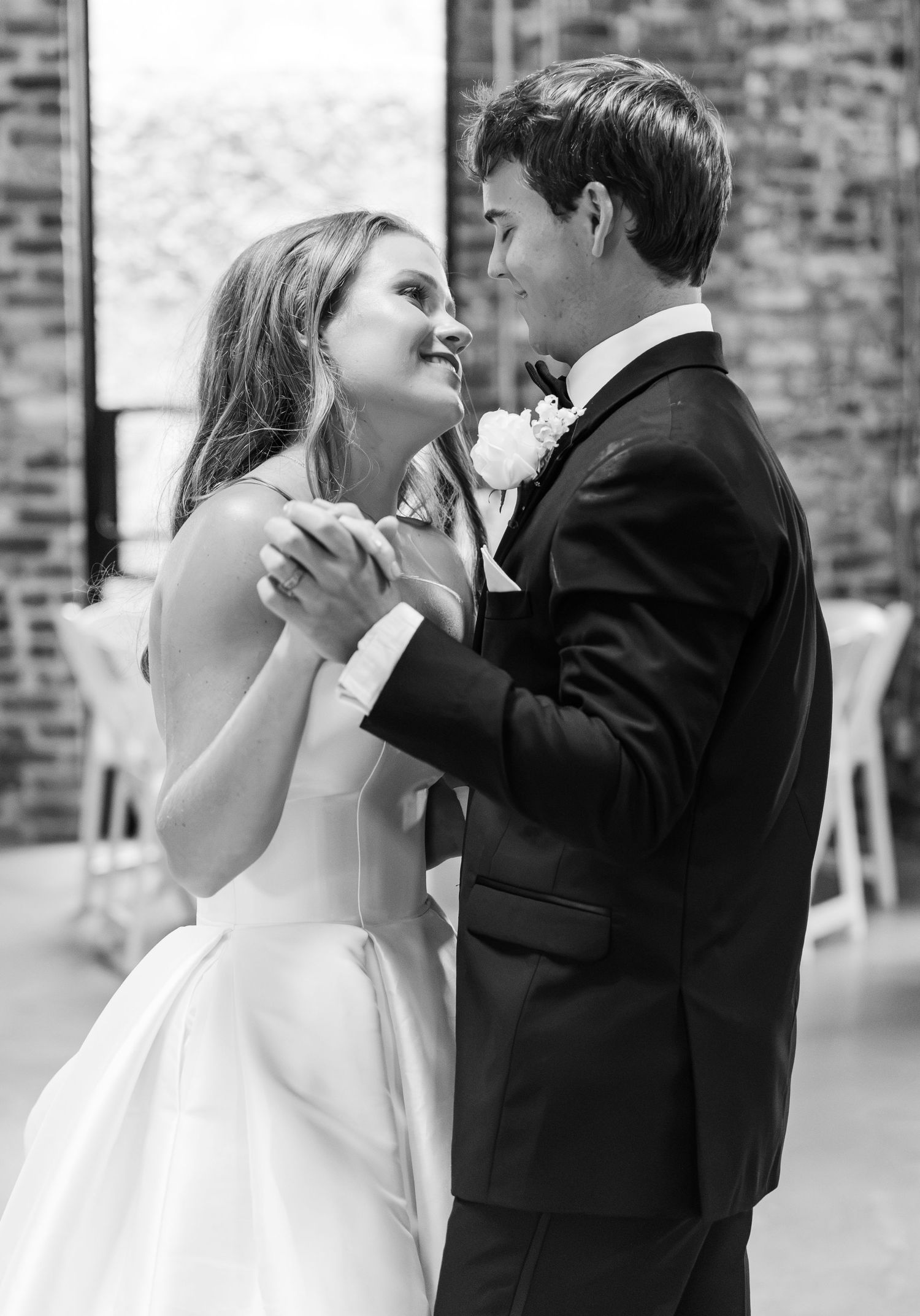 Black and white photo of newlyweds sharing their first dance, smiling lovingly at each other.