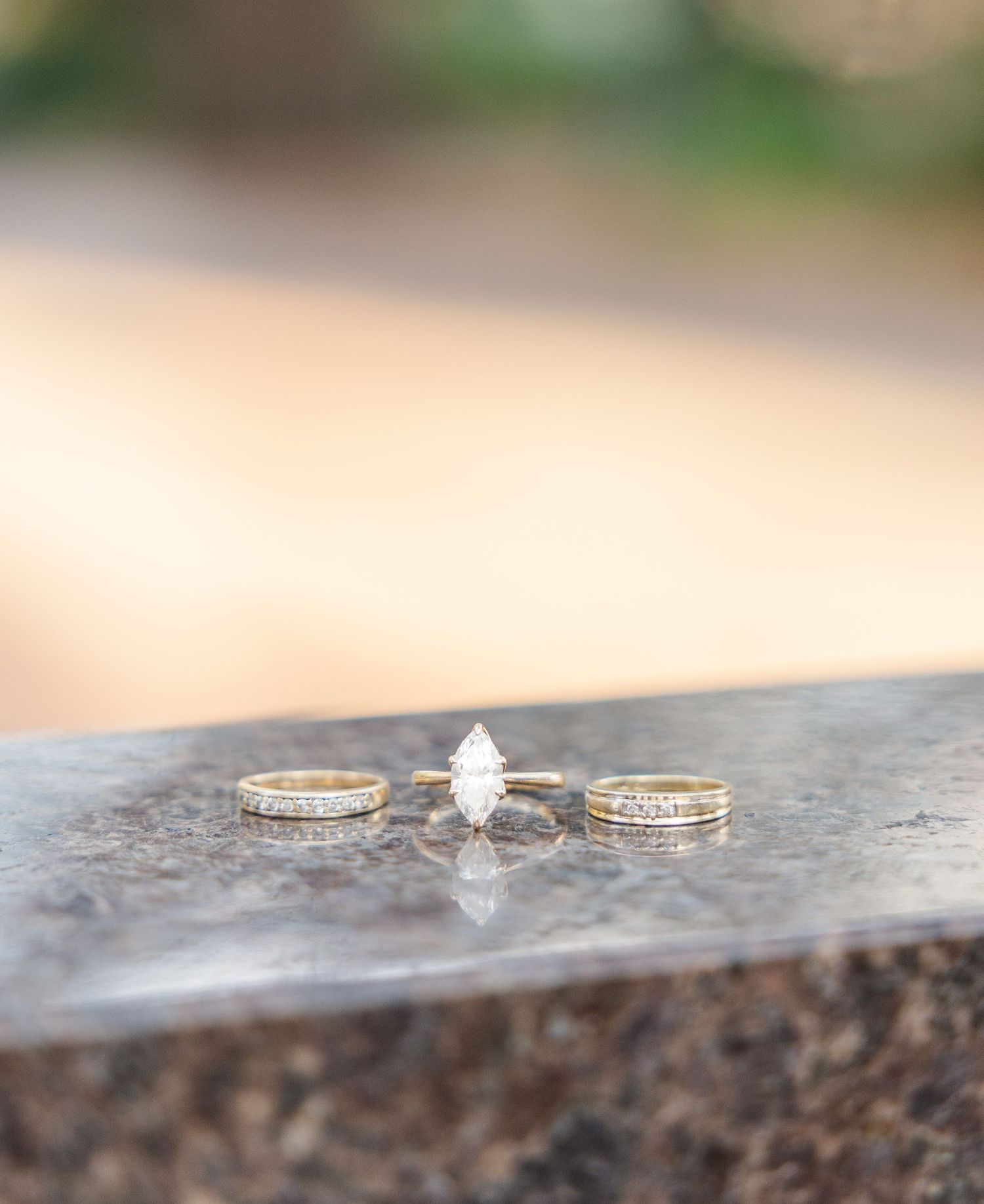 Gold engagement ring with marquise diamond flanked by two diamond wedding bands displayed on a stone surface.