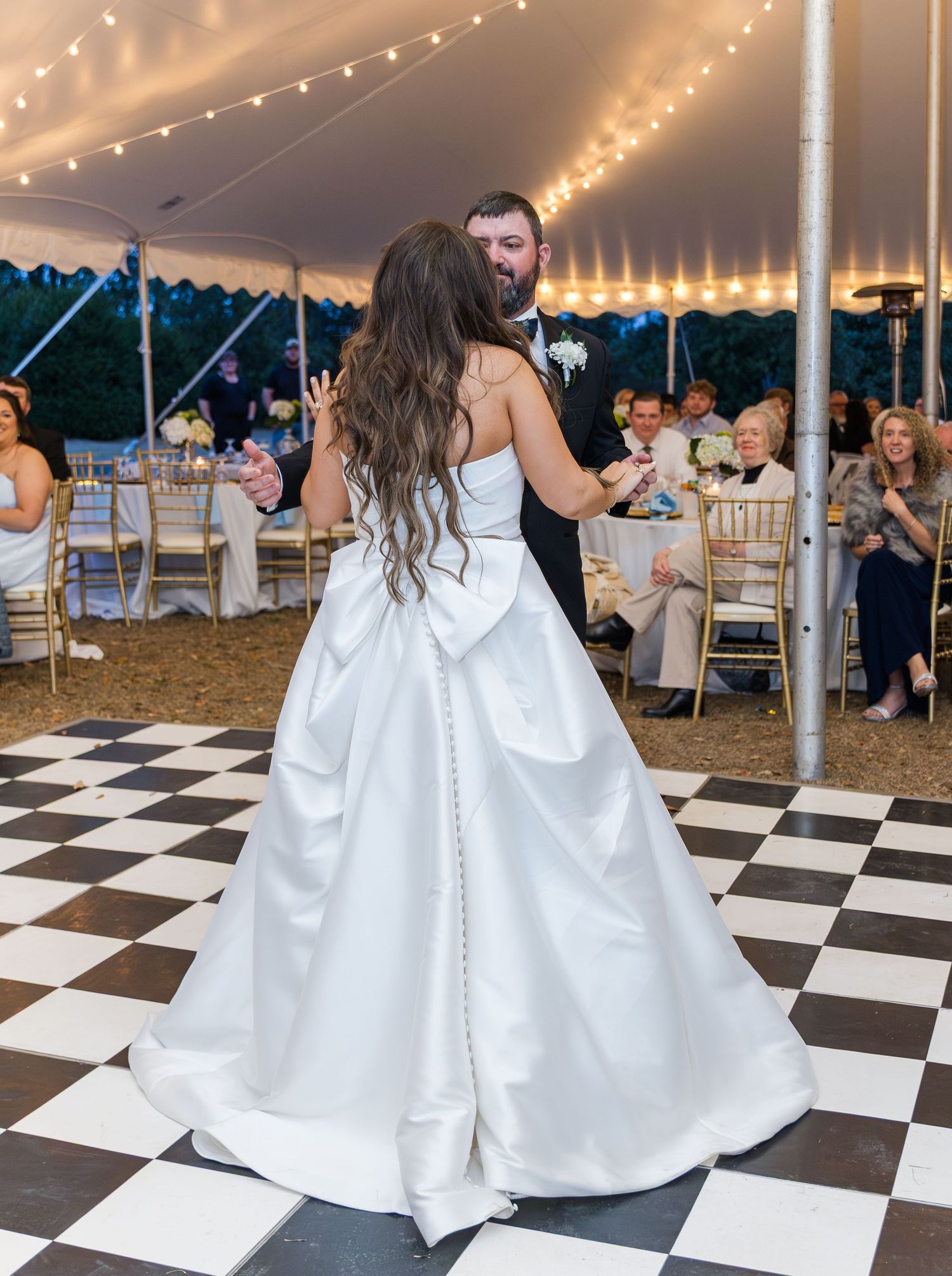 Bride and groom share their first dance under a tented reception with string lights and checkered floor.