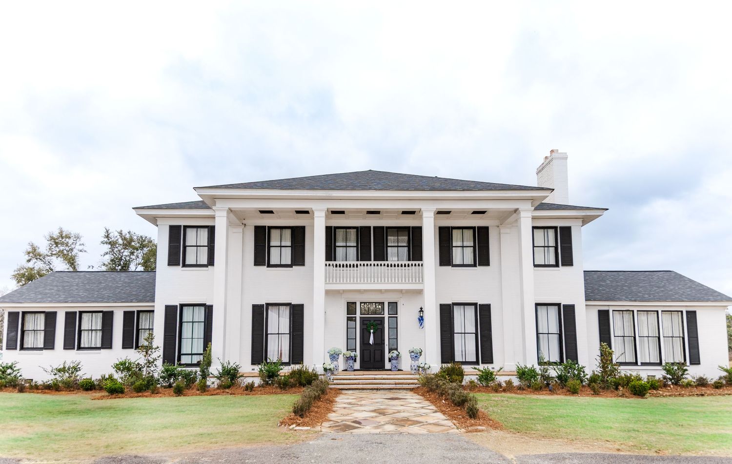 White Southern colonial wedding venue with black shutters, columns, and manicured landscaping.