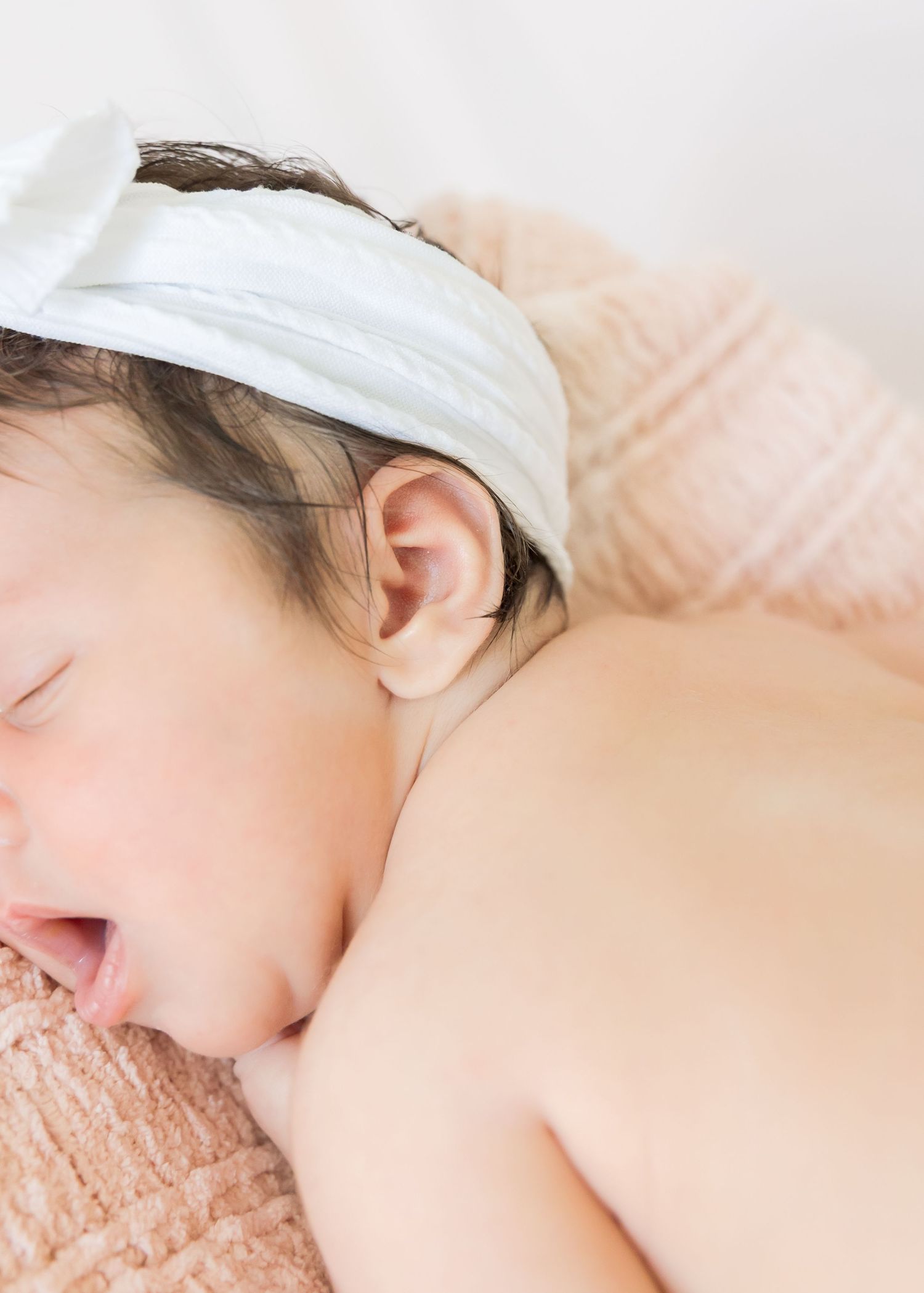 Close up of sleeping infant with white headband on pink textured fabric.