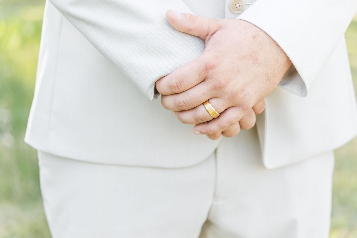 Close-up of groom's hands showing wedding band against crisp white suit.