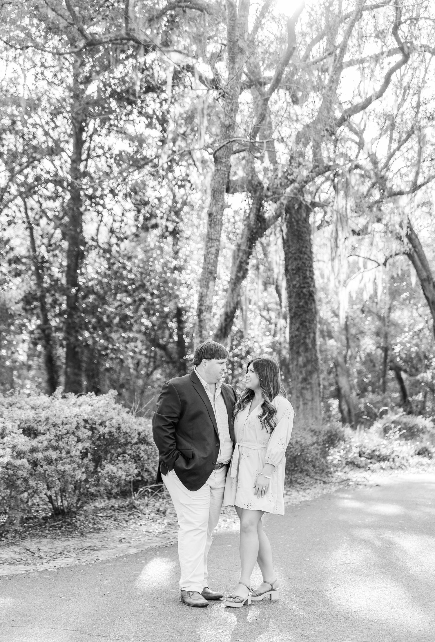 Black and white engagement portrait of a couple on a tree-lined path.