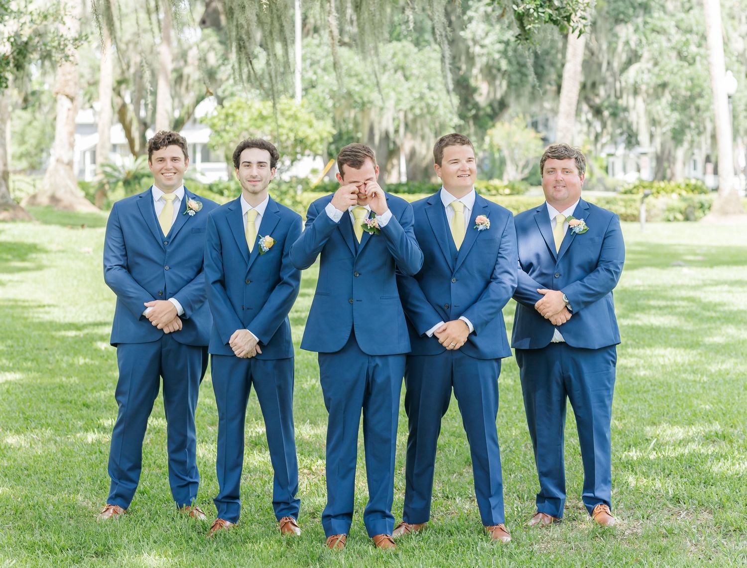 Groomsmen in matching navy blue suits posing on green lawn.