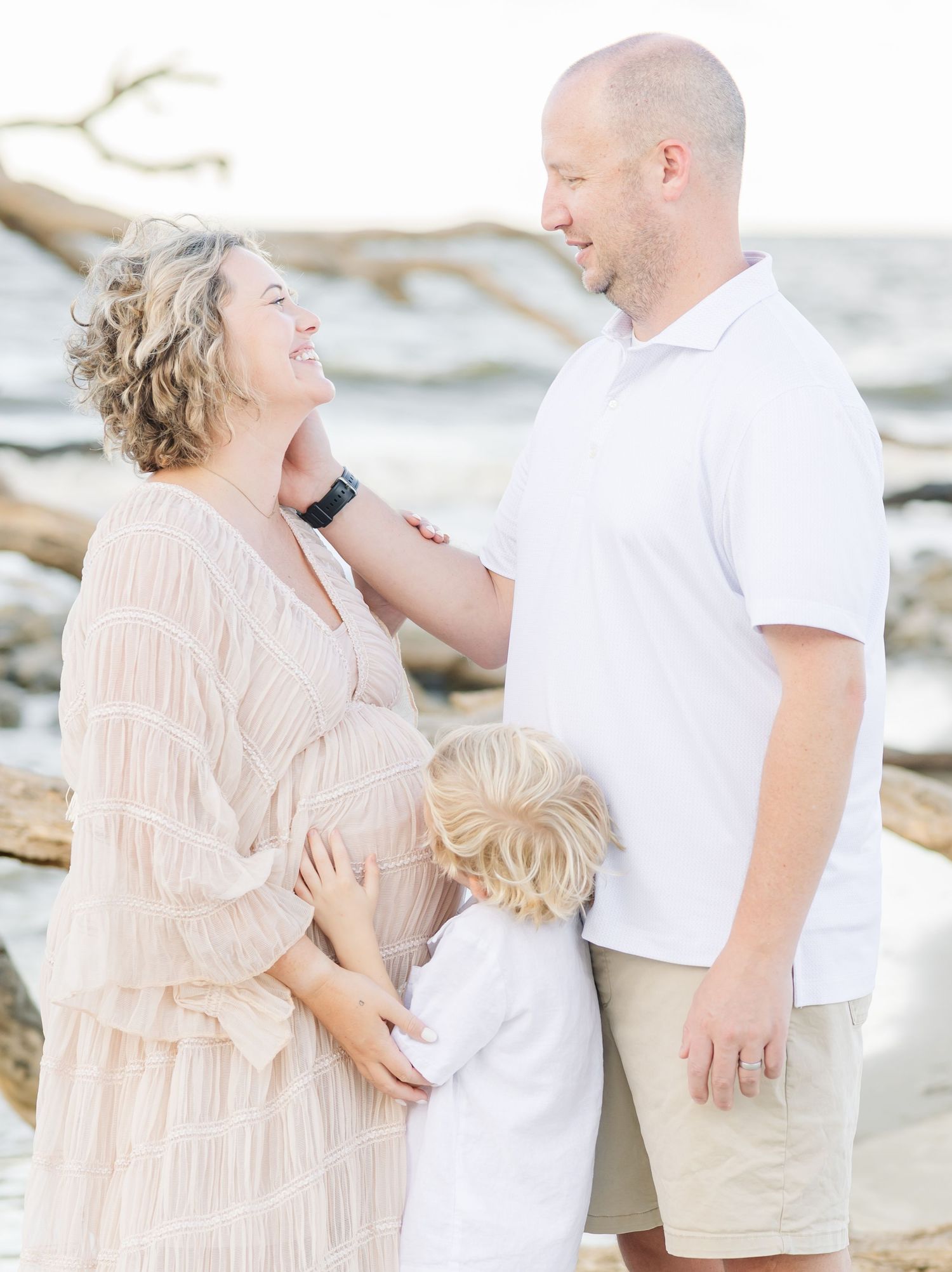A family shares a joyful moment together on a beach with driftwood in the background.