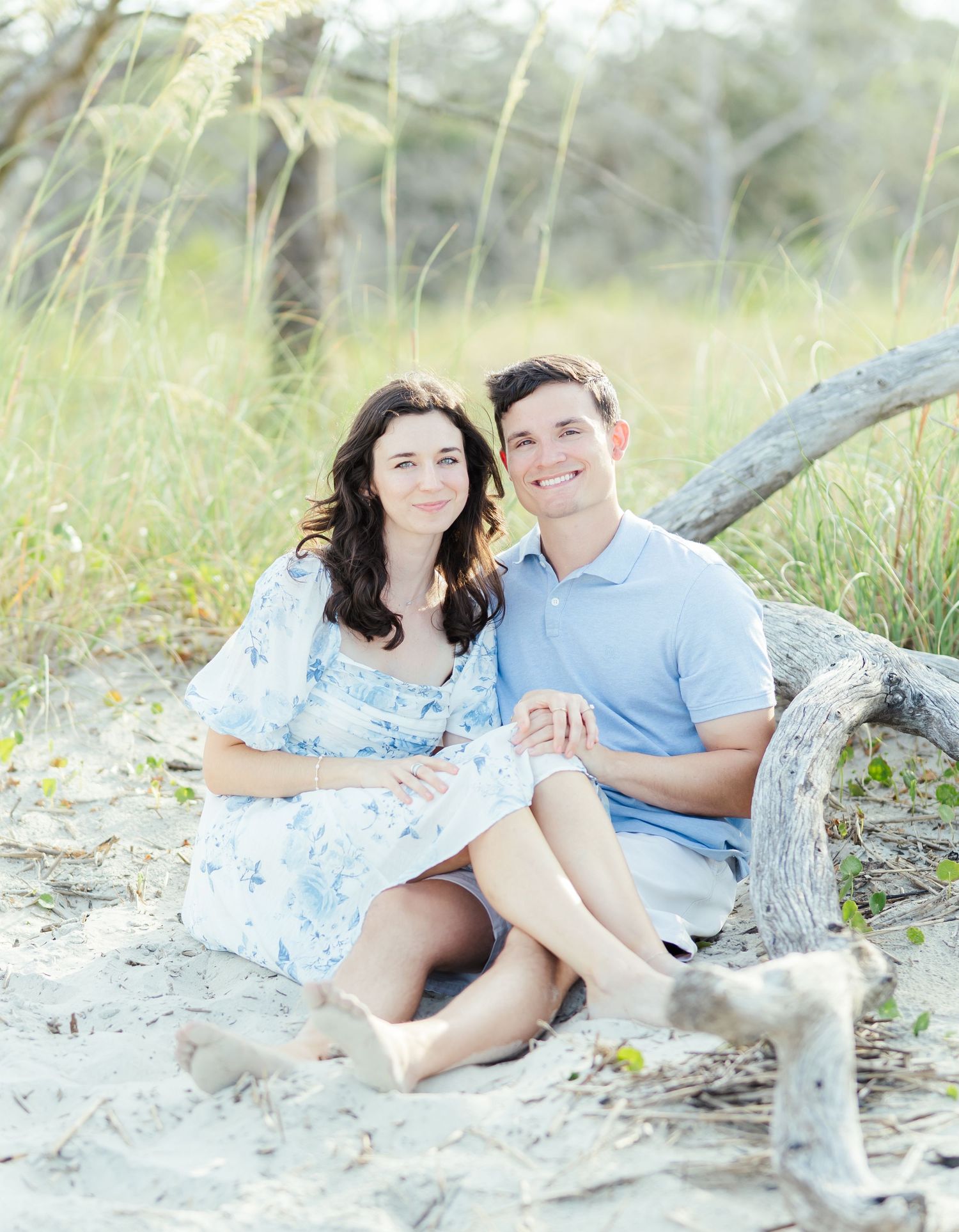 Couple relaxes on driftwood at the beach wearing coordinated blue and white outfits for a photo session.