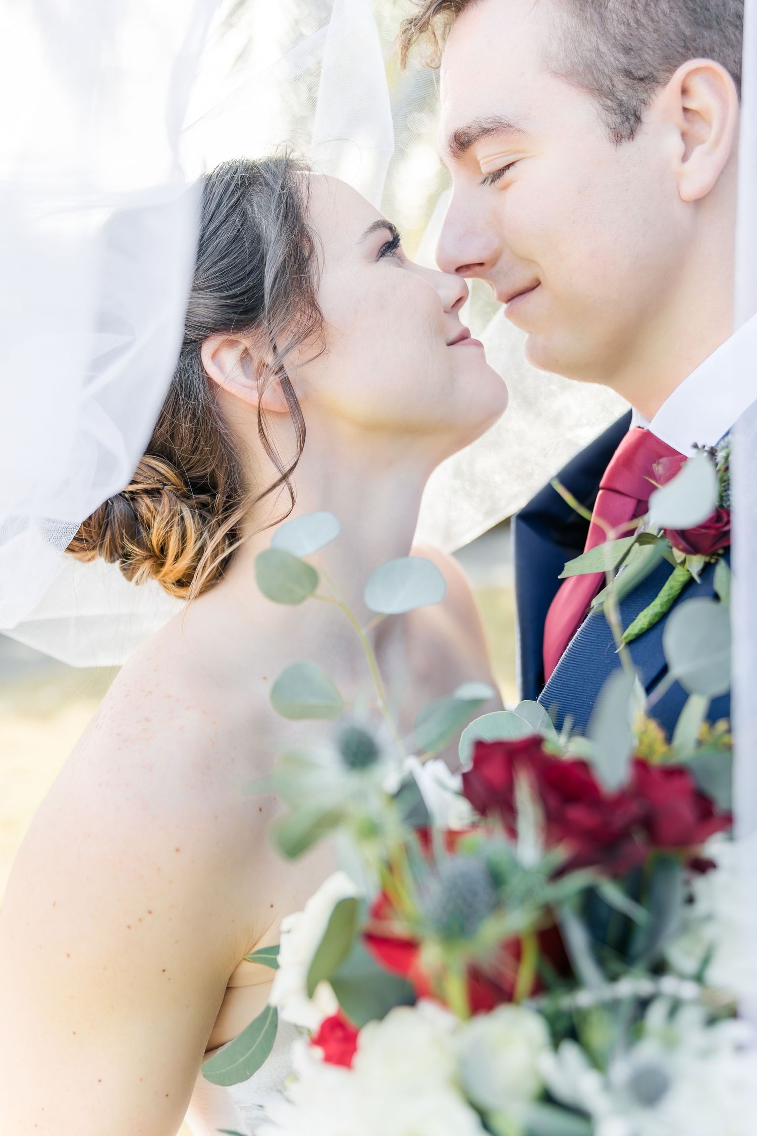 Romantic wedding portraits with eucalyptus and red roses in soft lighting.