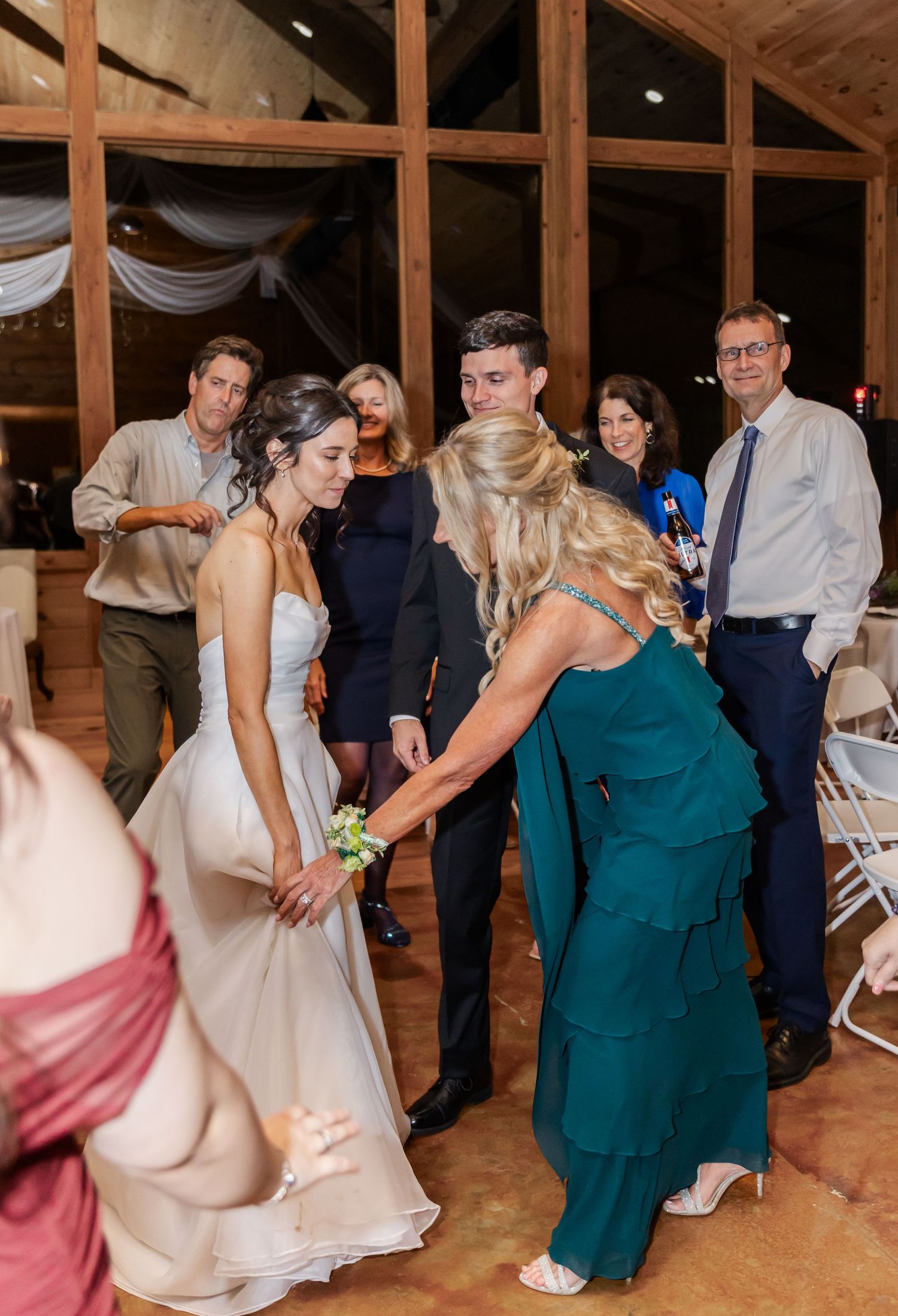 Wedding guests dancing and celebrating on a rustic wooden dance floor at an indoor barn reception venue.