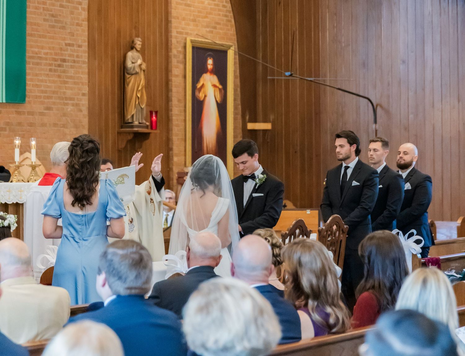 Church wedding ceremony with guests seated in wooden pews and green shutters on brick walls.