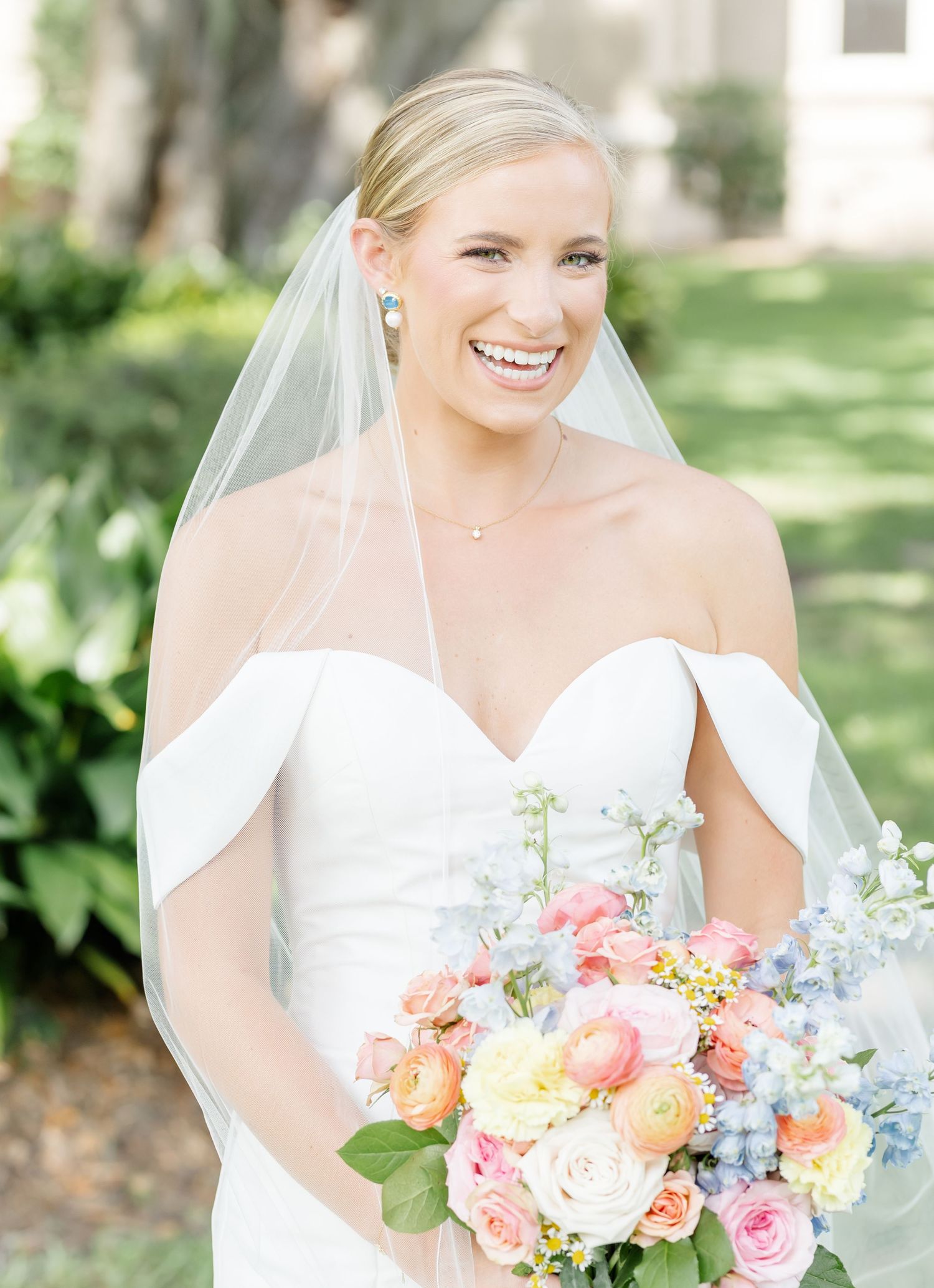 A wedding bouquet featuring pastel pink roses, coral blooms, and delicate blue flowers creates a romantic spring arrangement.