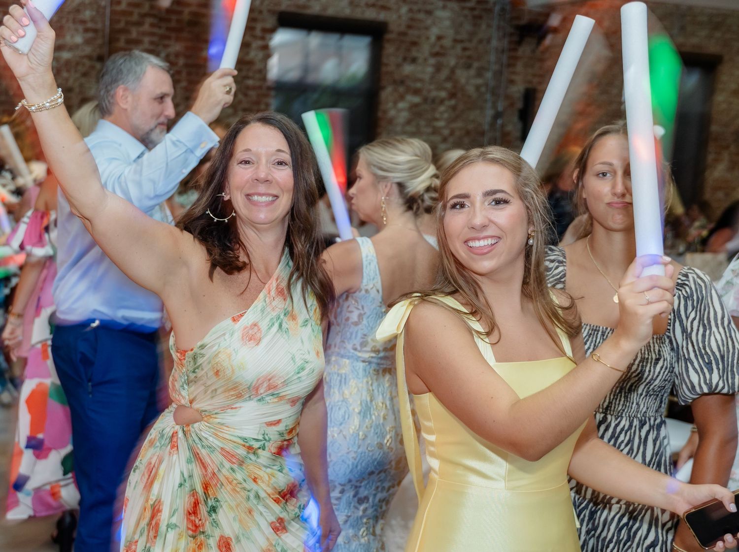 Wedding guests dancing and celebrating on a crowded dance floor with colorful lighting and festive atmosphere.