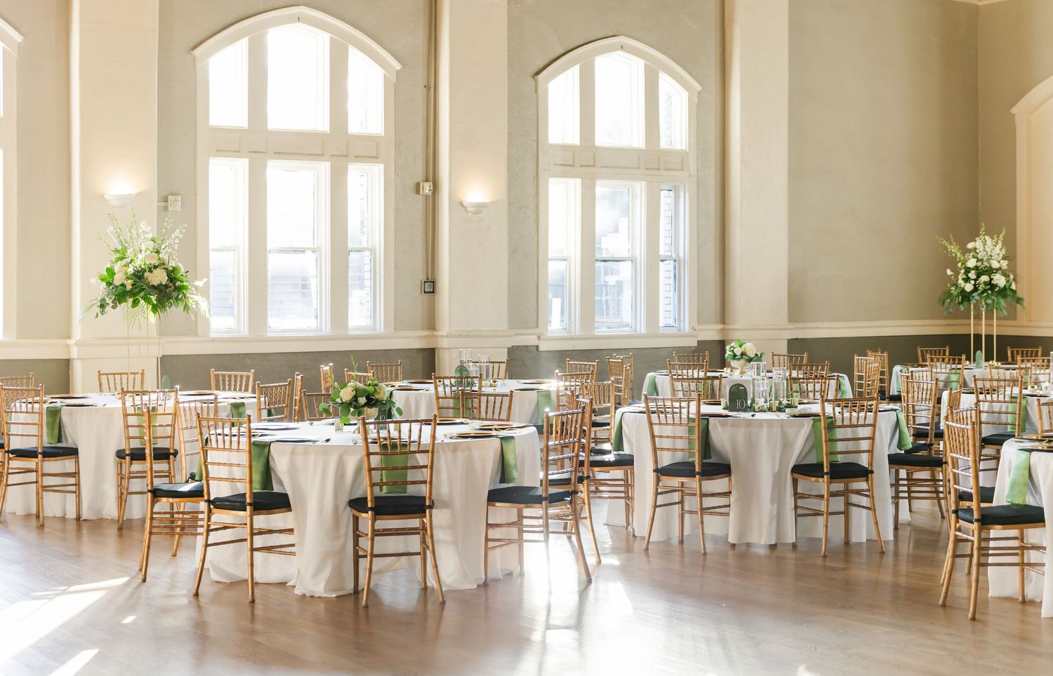 Elegant reception venue with high arched windows and tables set with mint green accents.