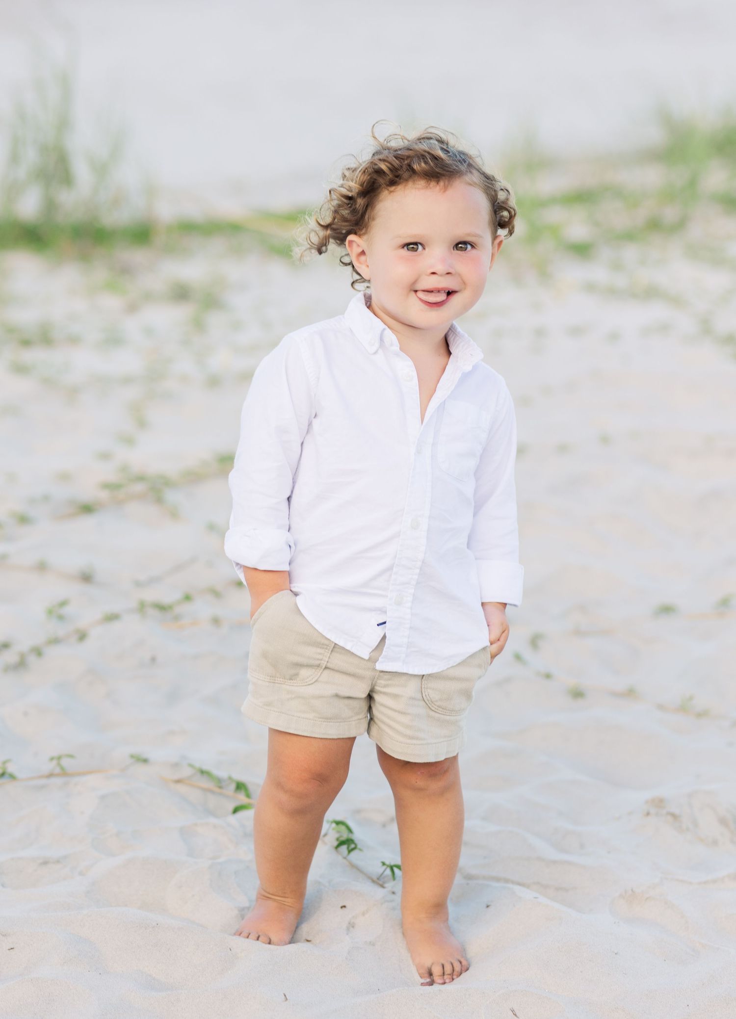 A white button-down shirt and khaki shorts outfit being modeled on a sandy beach.