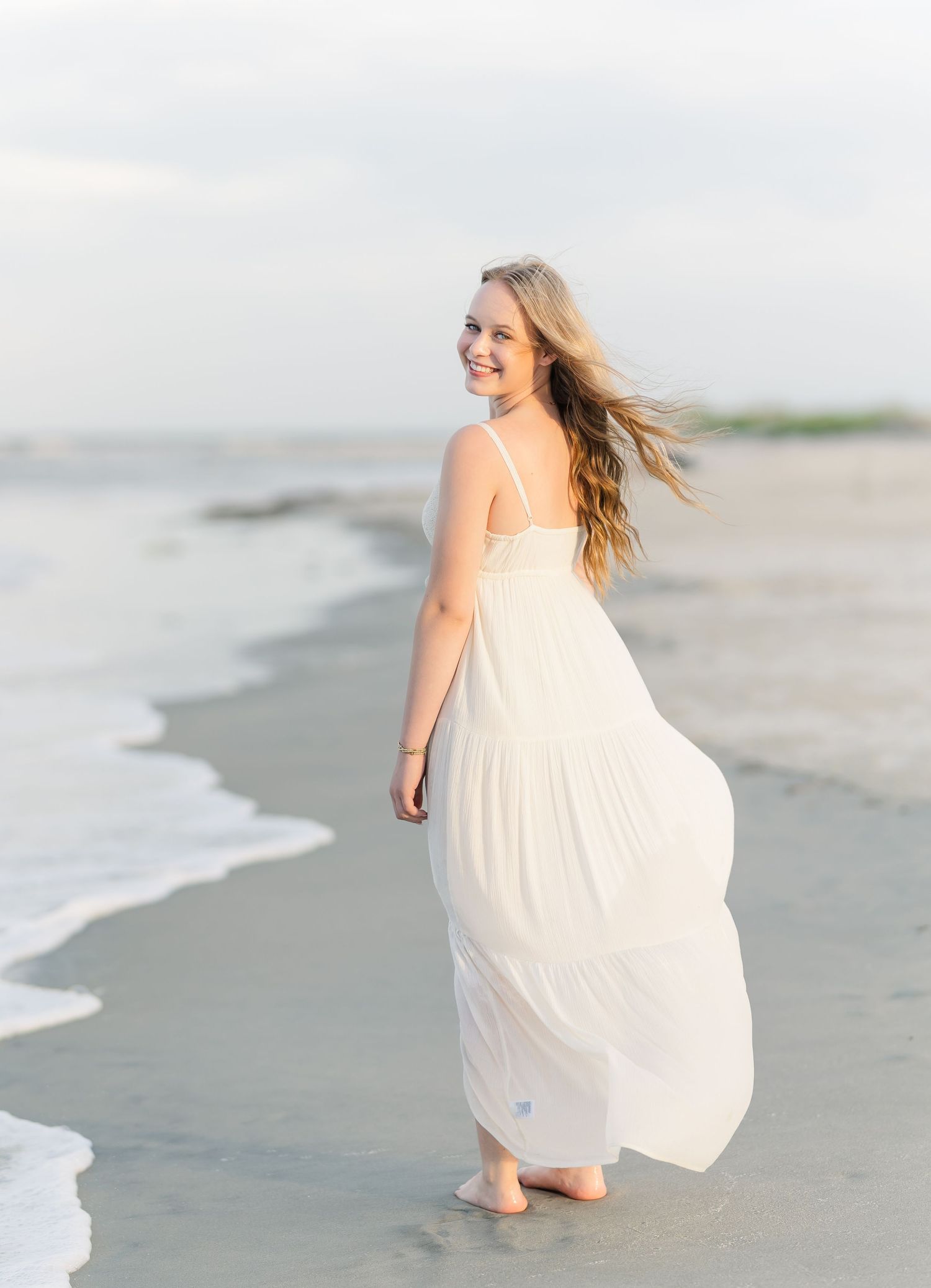 A flowing white dress catches the sea breeze during a sunset beach photoshoot.